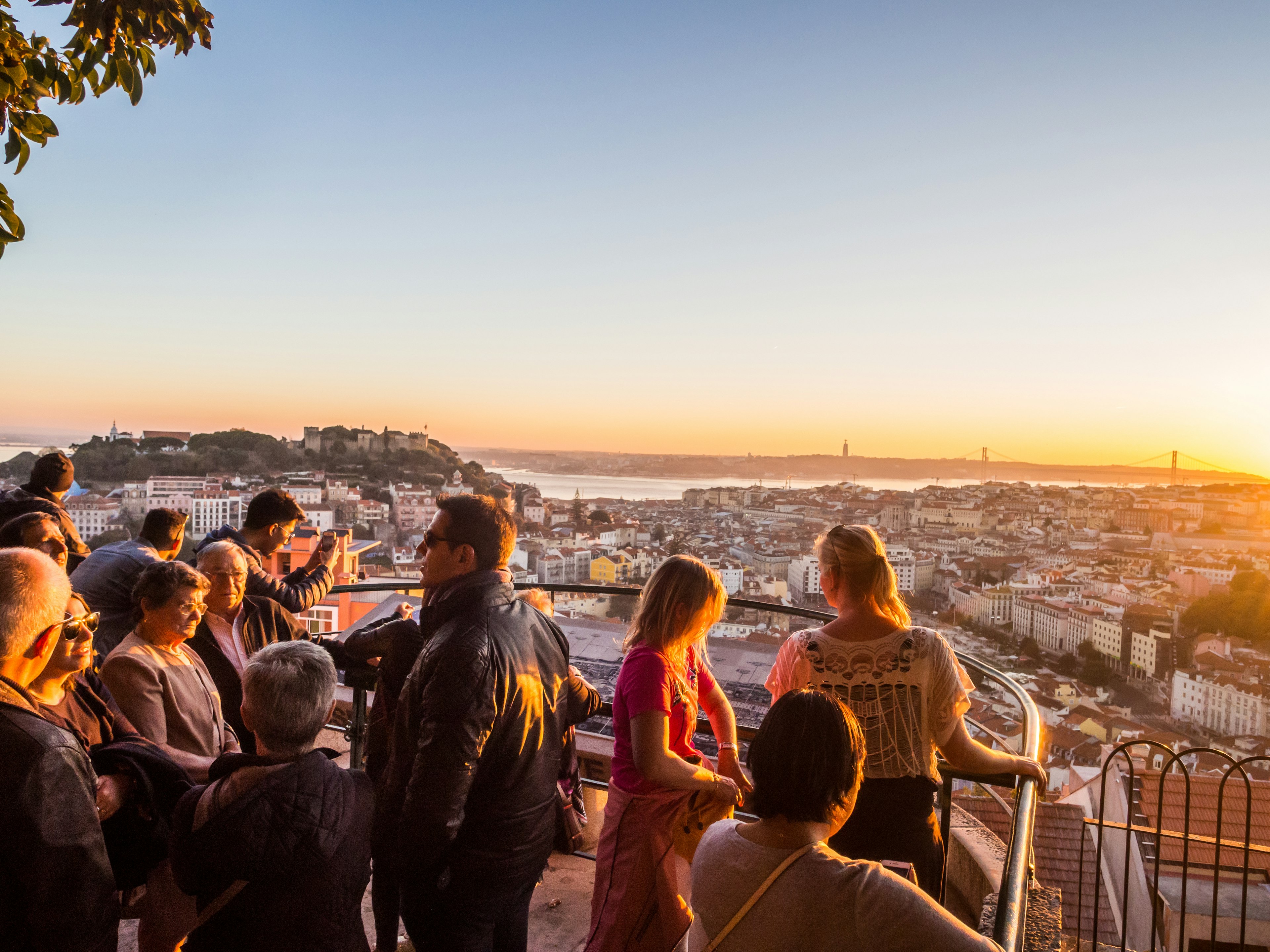 Tourists at Belvedere of Our Lady of the Hill viewpoint, looking at the cityscape of Lisbon at sunset.