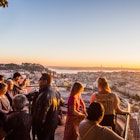 Tourists at Belvedere of Our Lady of the Hill viewpoint, looking at the cityscape of Lisbon at sunset.