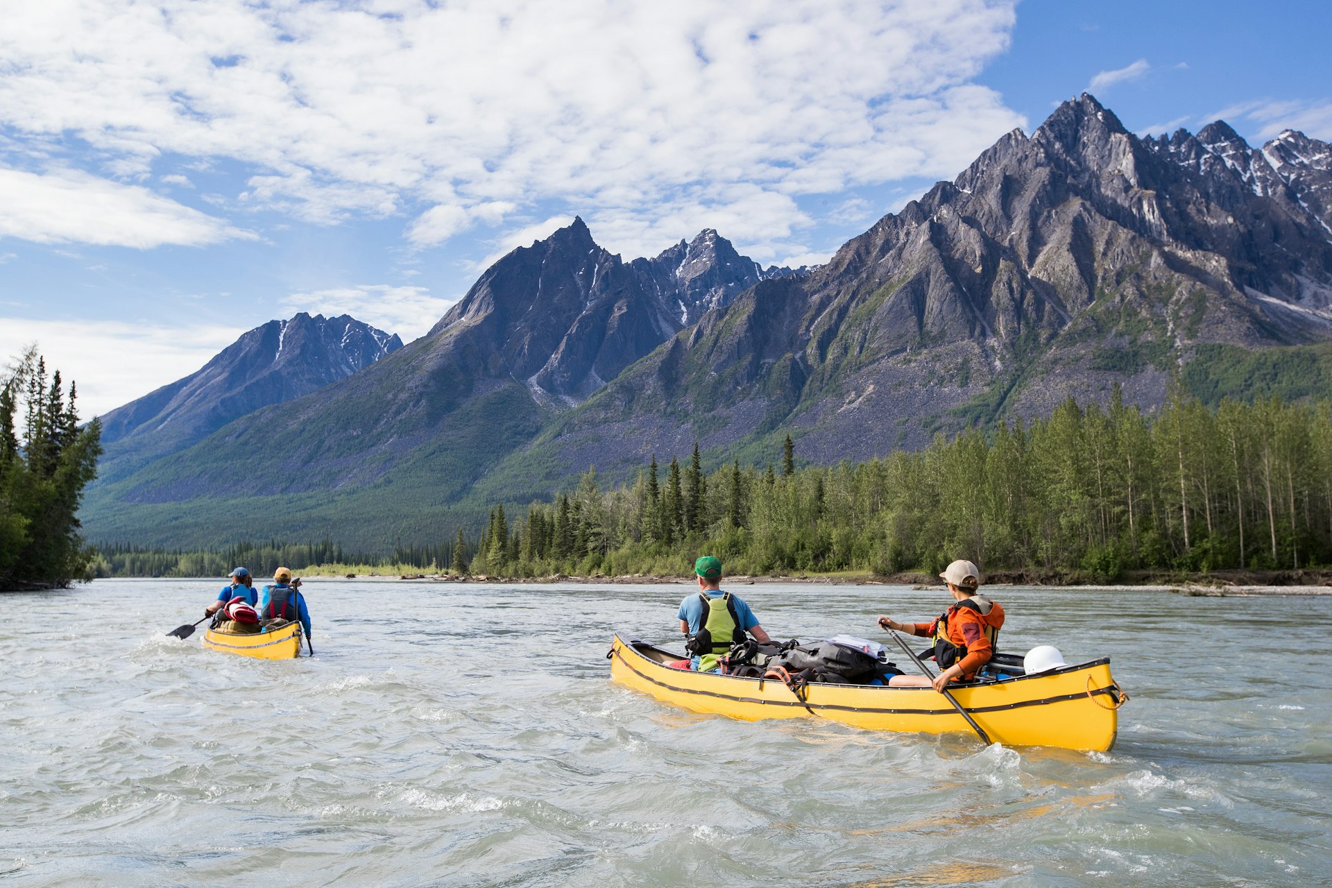 People in two canoes paddle down a river in a mountainous region