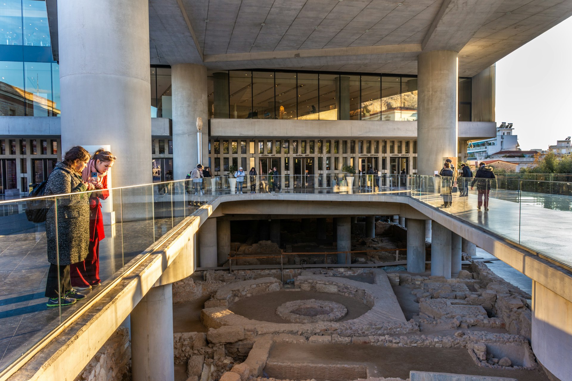 Entrance of the Acropolis Museum in Athens with two women looking at the excavated site from a bridge, Greece