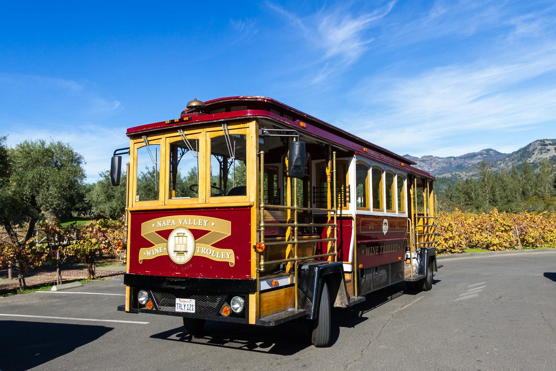 A cable car that's been converted to run on the road parked near a vineyard