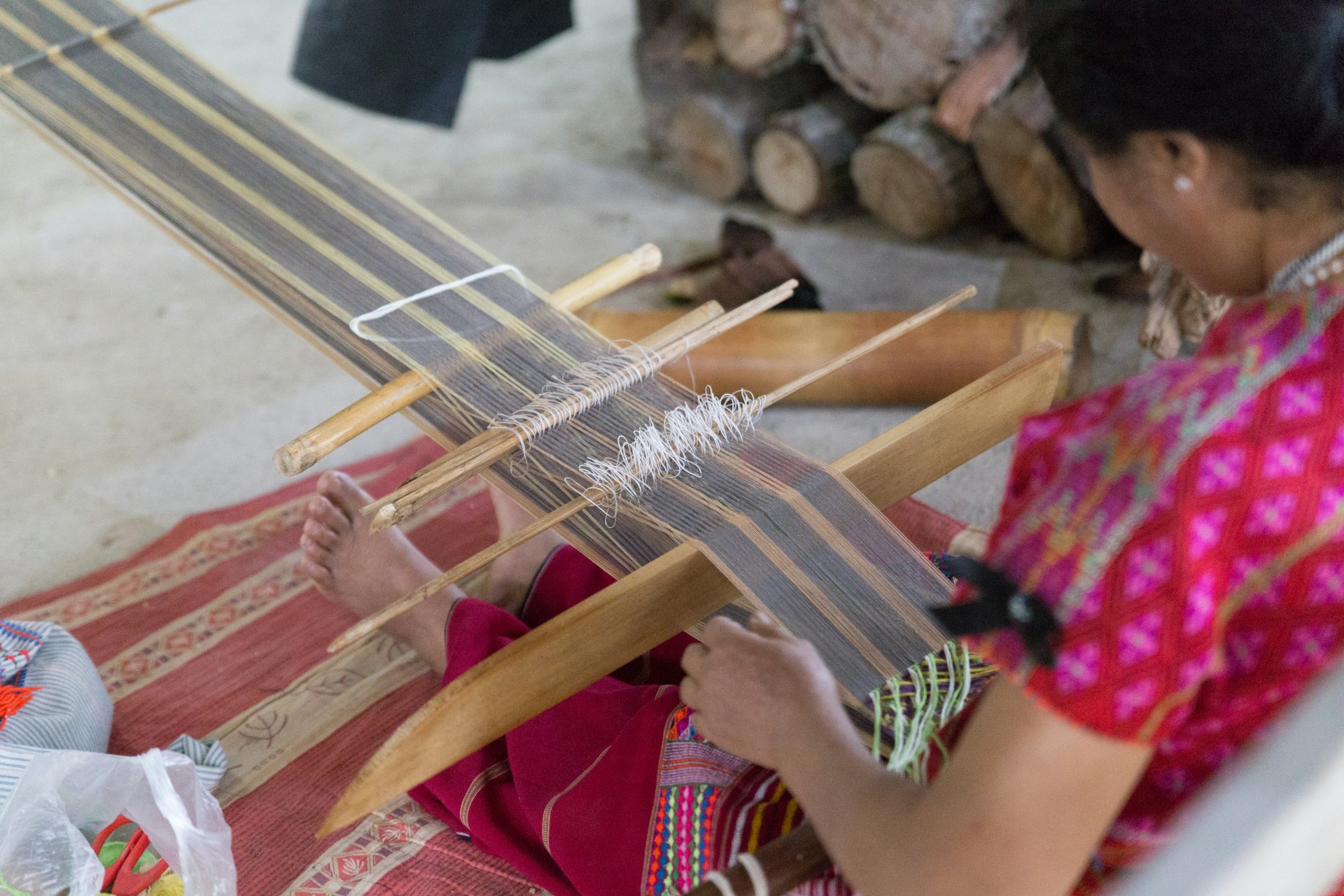A woman is sitting on the floor and using a traditional loom to weave fabric