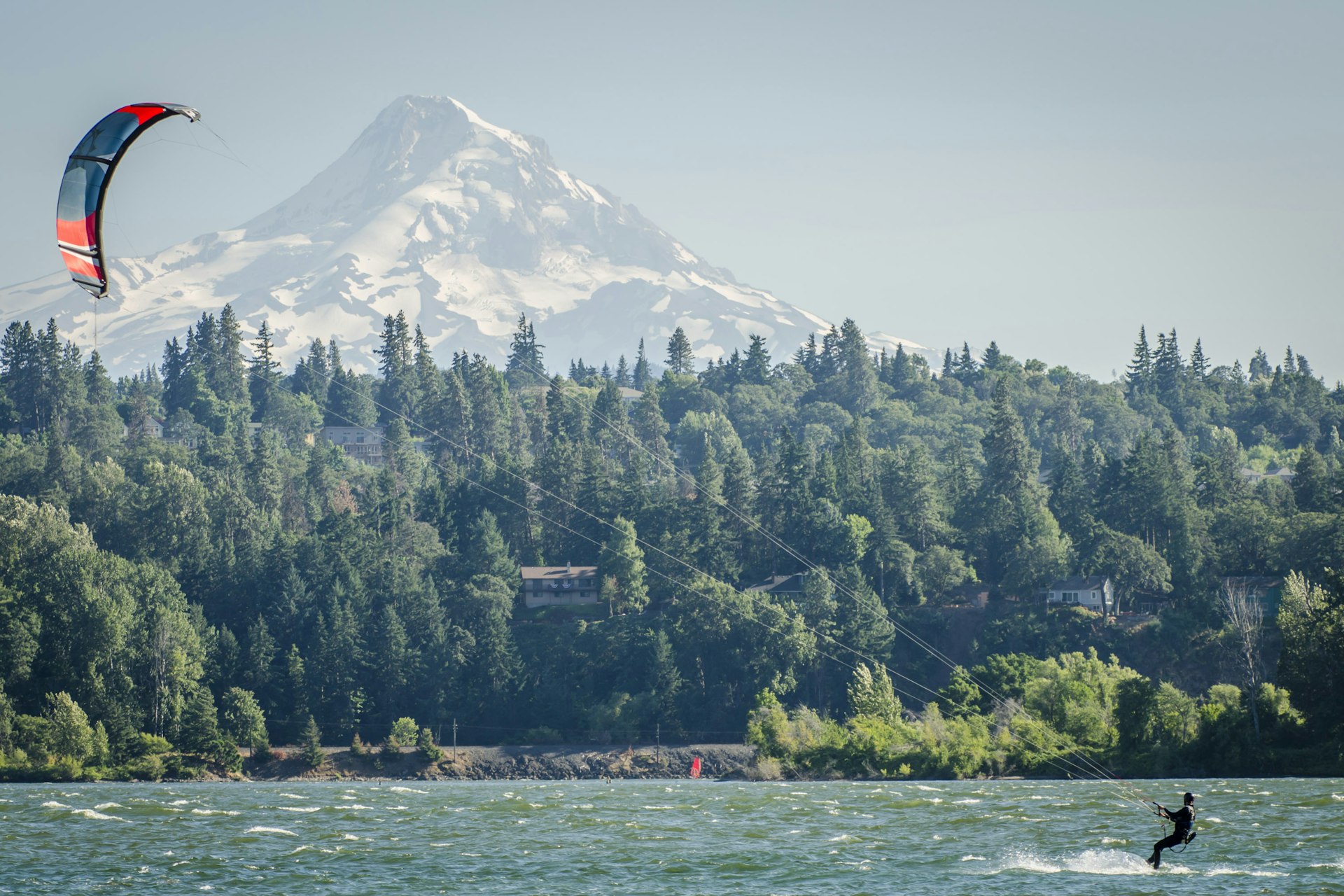 A person kiteboards on the Columbia River with green trees and Mt Hood in the distance, Oregon, USA
