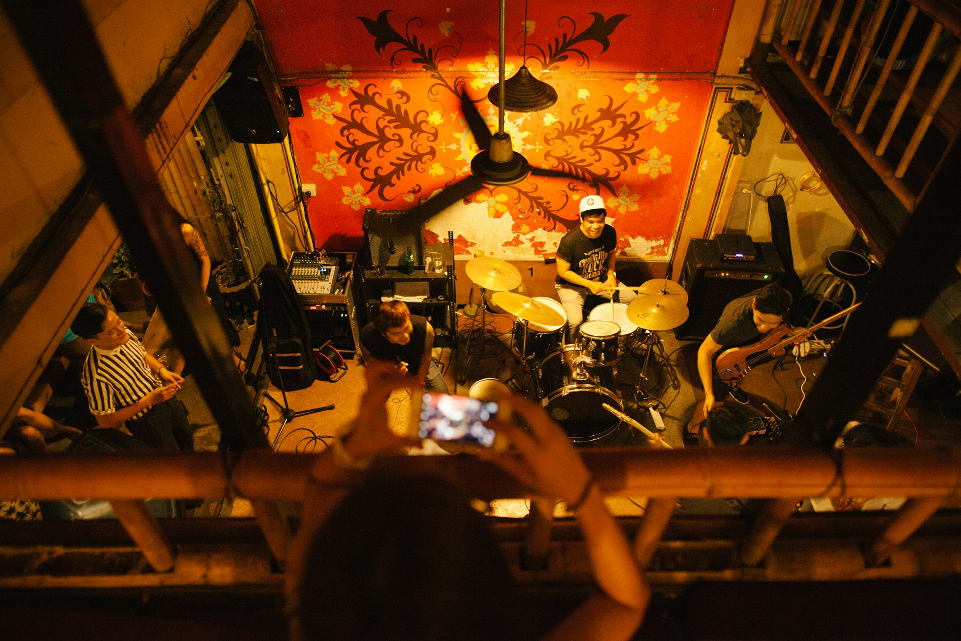 A gig-goer is standing on a balcony and taking a photo of the band on stage below at North Gate Jazz Co-Op, Chiang Mai 