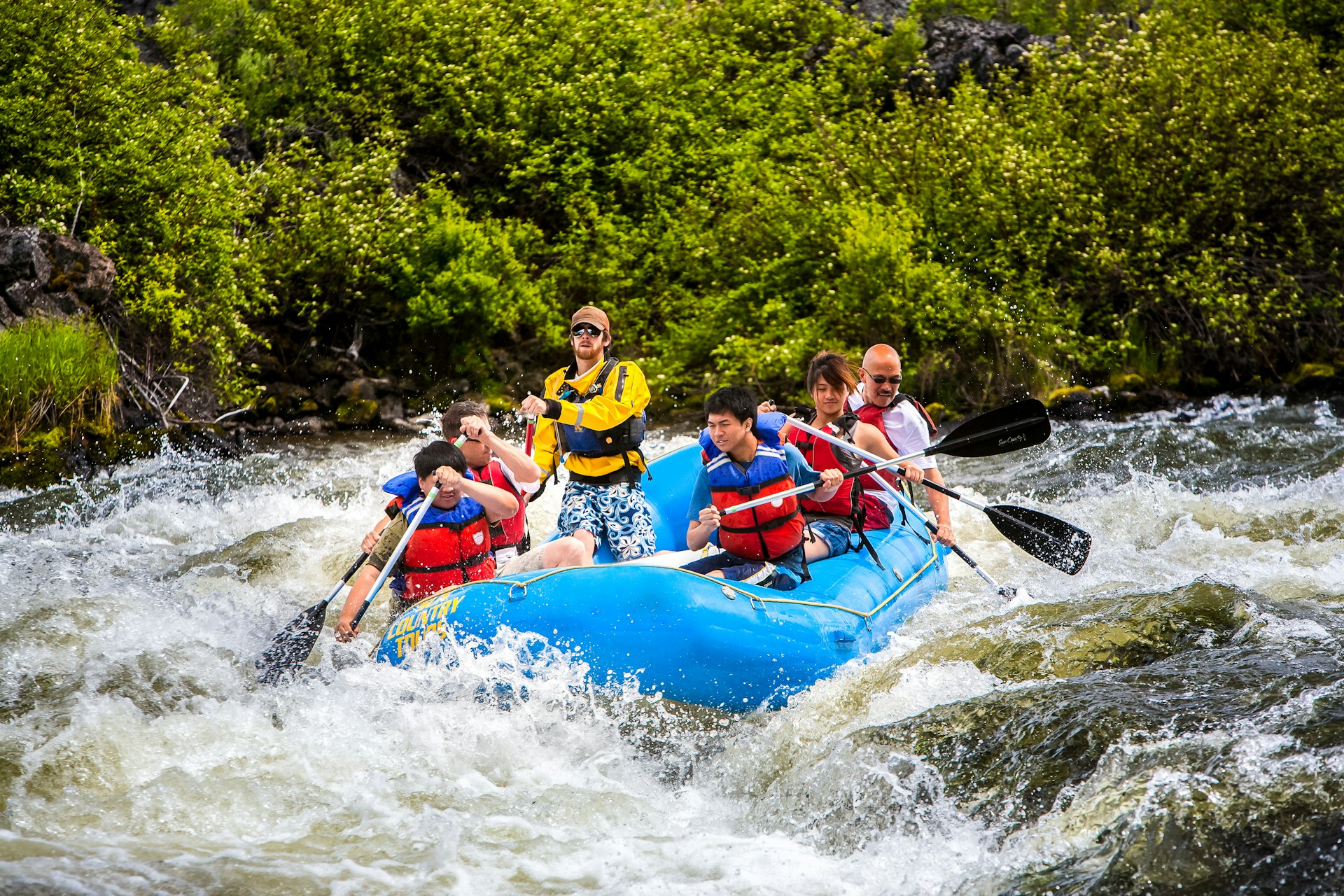 Rafters on a large raft tackle rapids in a river