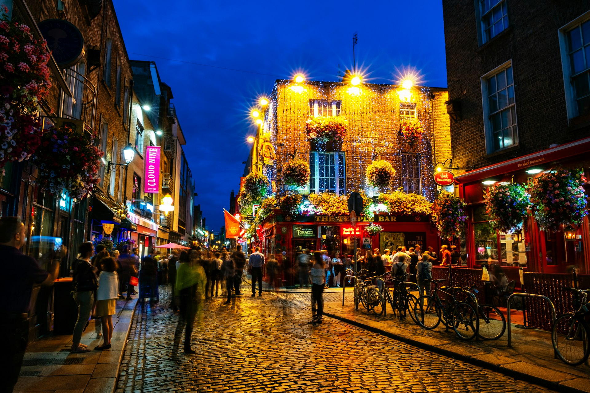 People enjoying nightlife on a cobbled street outside some pubs in a city