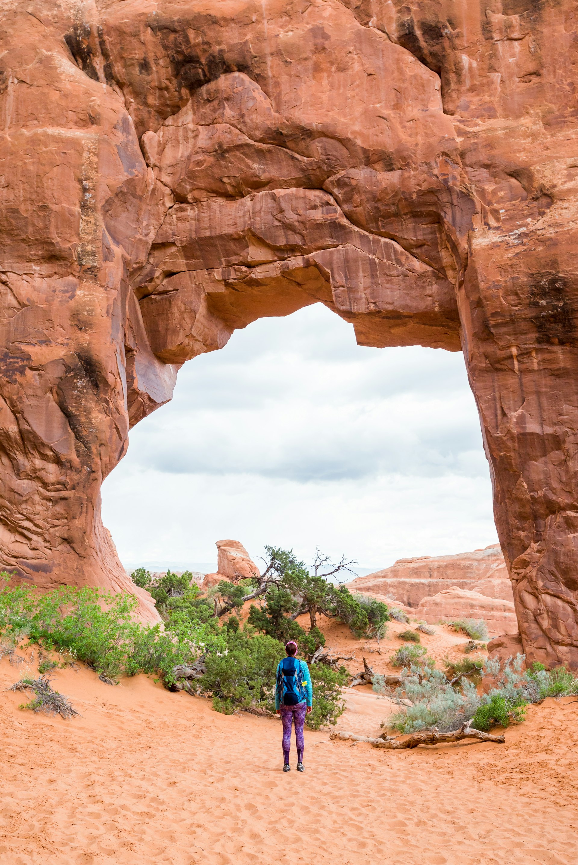 Female hiker is looking at the Pine Tree Arch at Devils Garden in the Arches National Park.