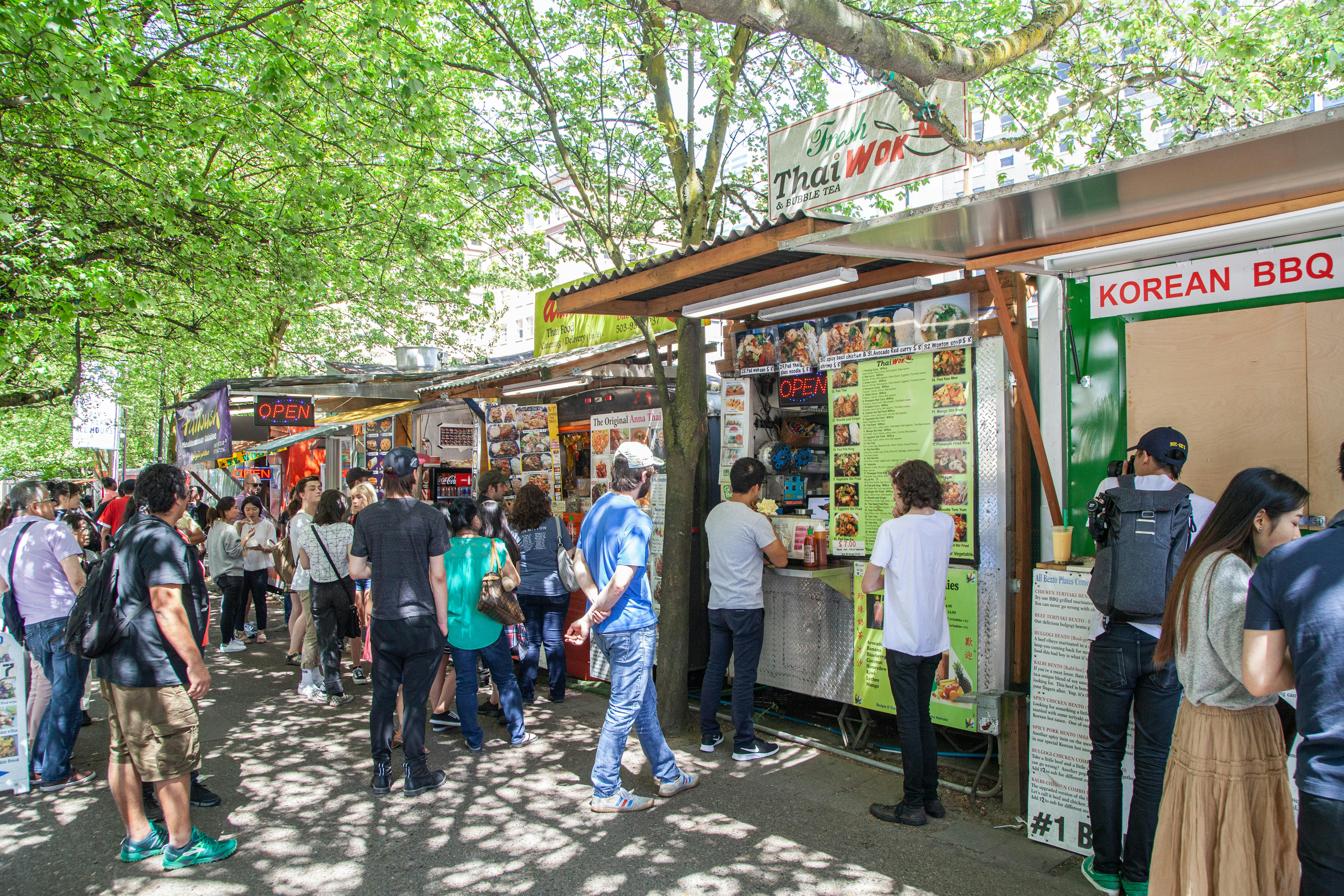 People line up in front of various street food stalls selling Thai and Korean BBQ food