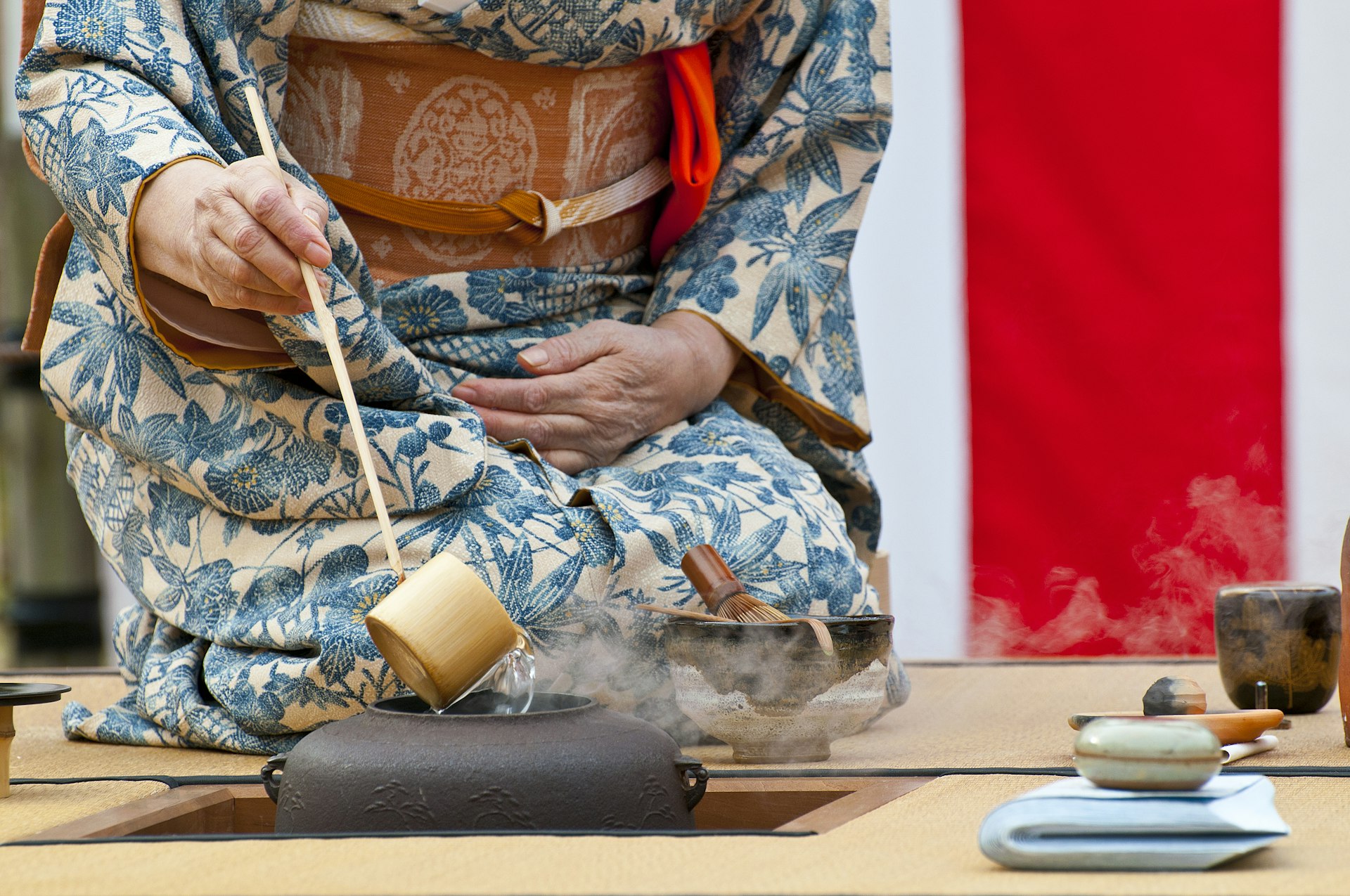A person wearing a kimono kneels as they pour hot water