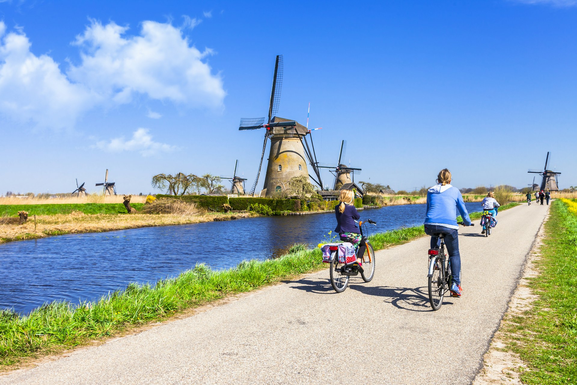 Mother and children ride bicyles past windmills at Kinderdijk.