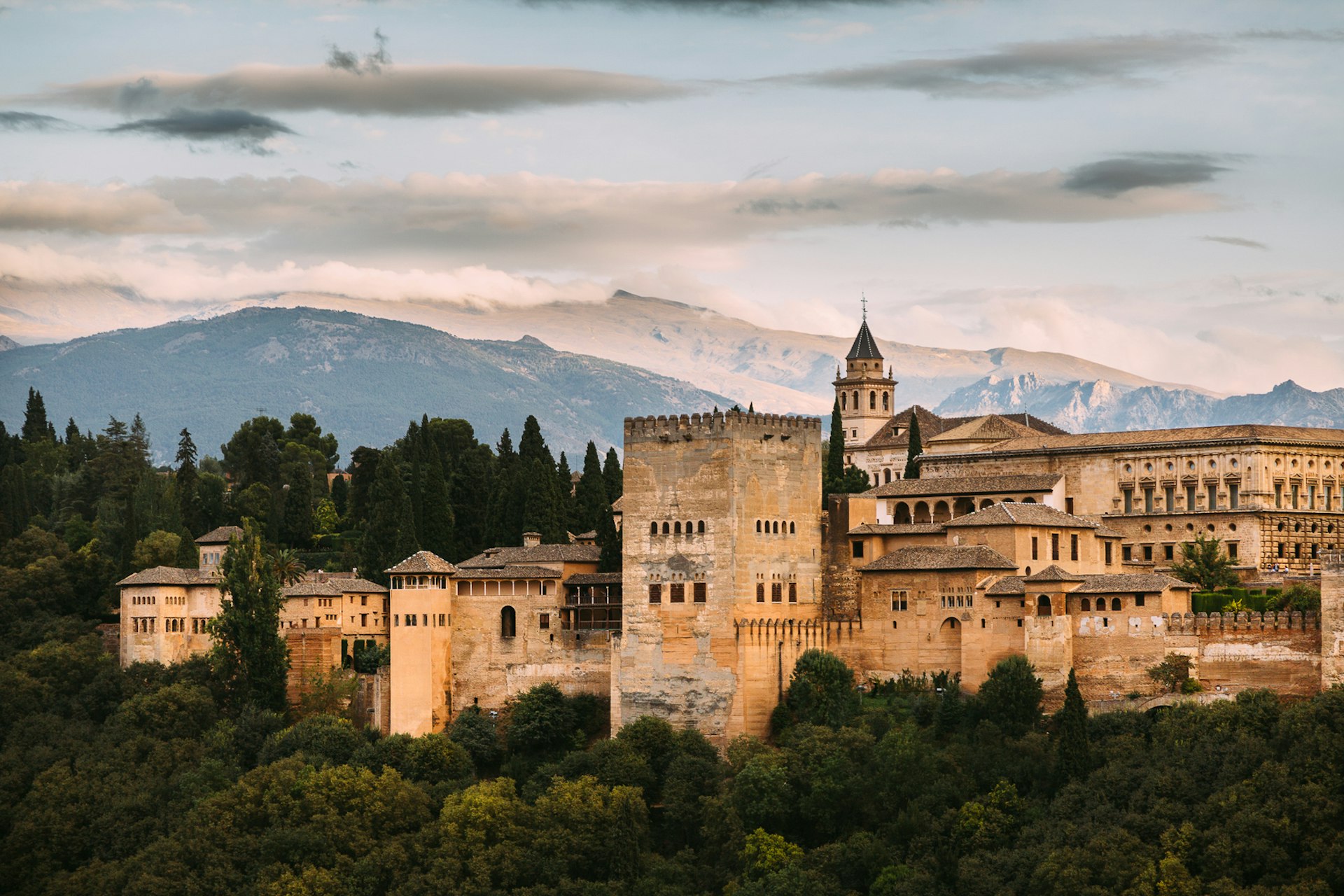 The large palace of the Alhambra sits on a hill with mountains in the background. 