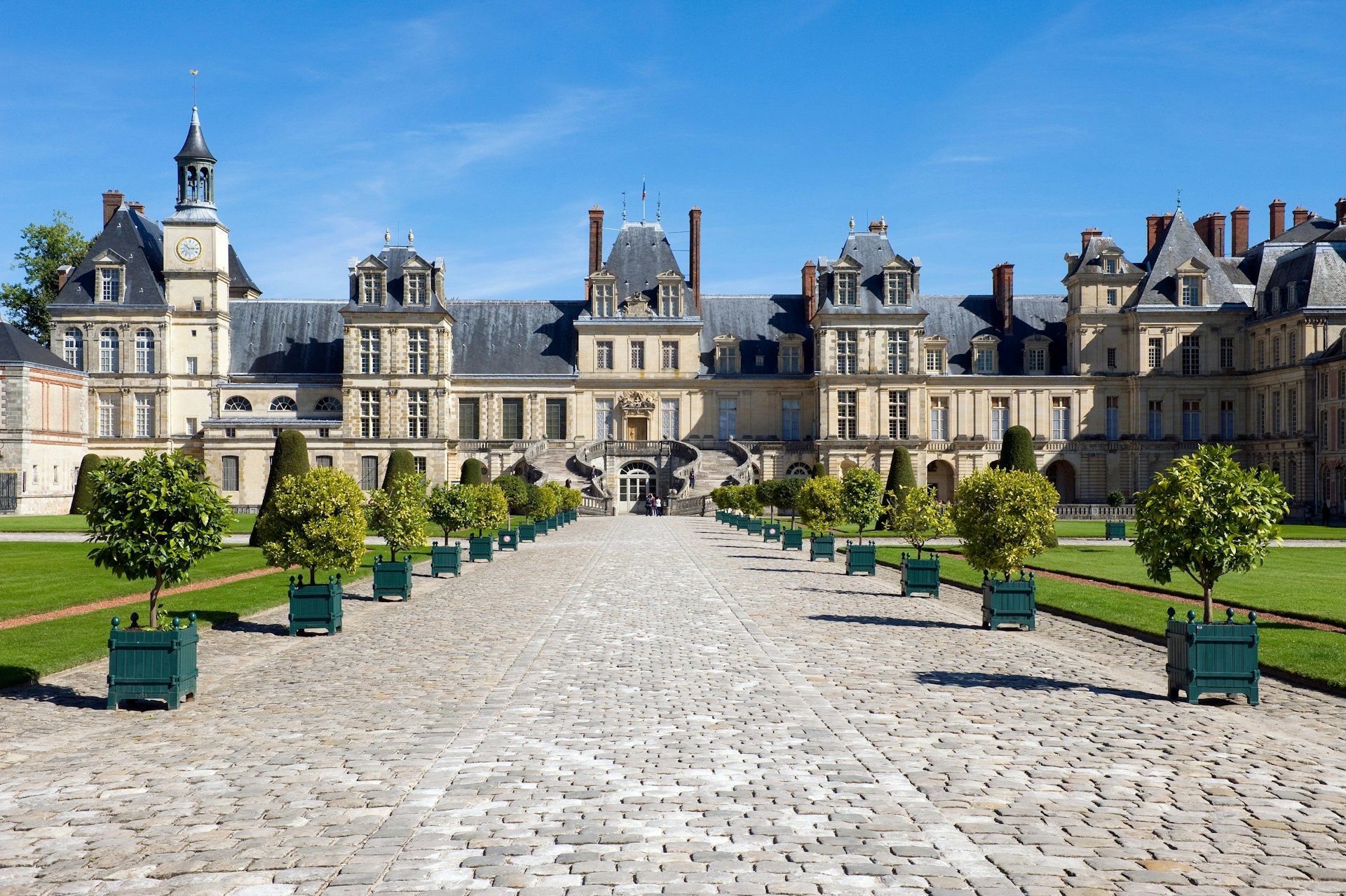 Planter-lined cobblestone pathway leading to Chateau Fontainebleau in France