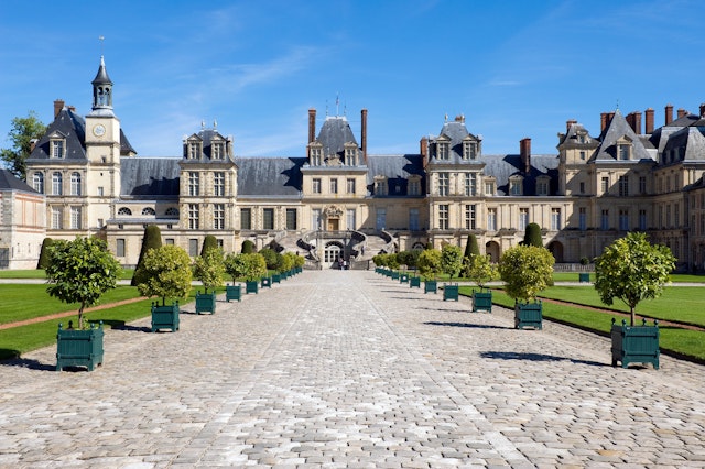 Planter-lined cobblestone pathway leading to Chateau Fontainebleau in France