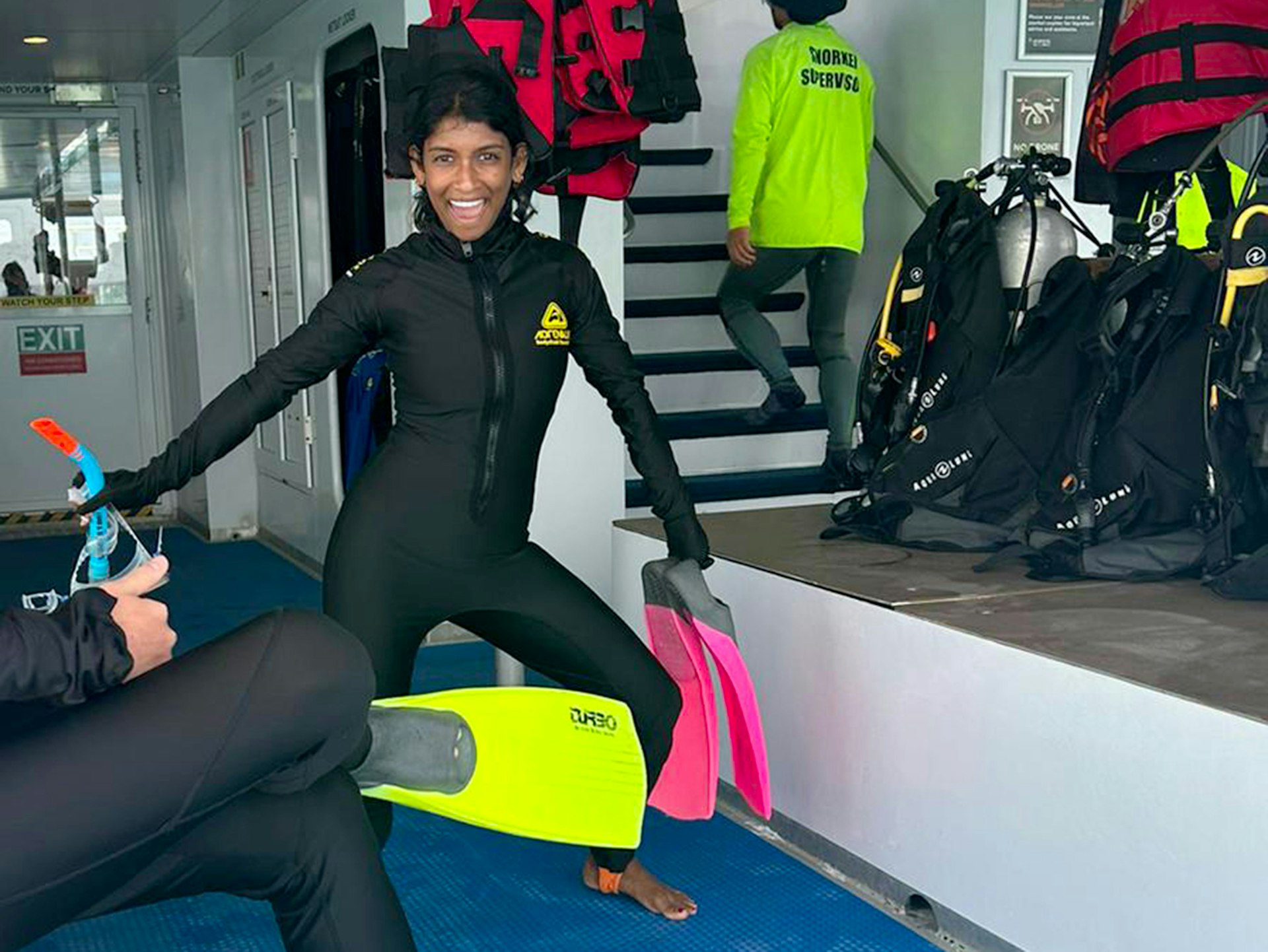 A woman on a dive boat smiles for the camera as she gets her scuba gear on