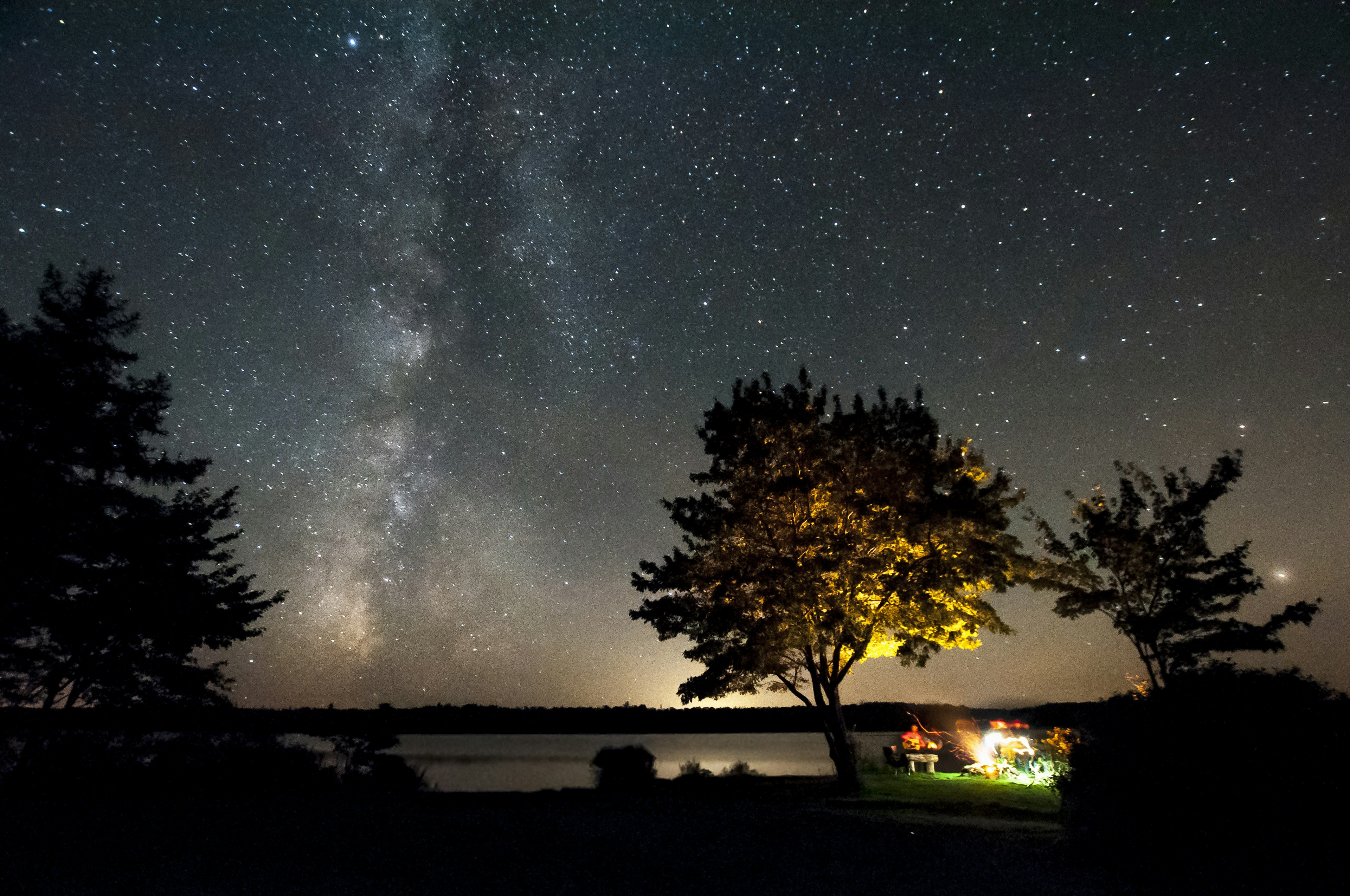 Nighttime shot of friends sitting at campfire underneath the Milky Way at Malay Falls, Nova Scotia, Canada Getty