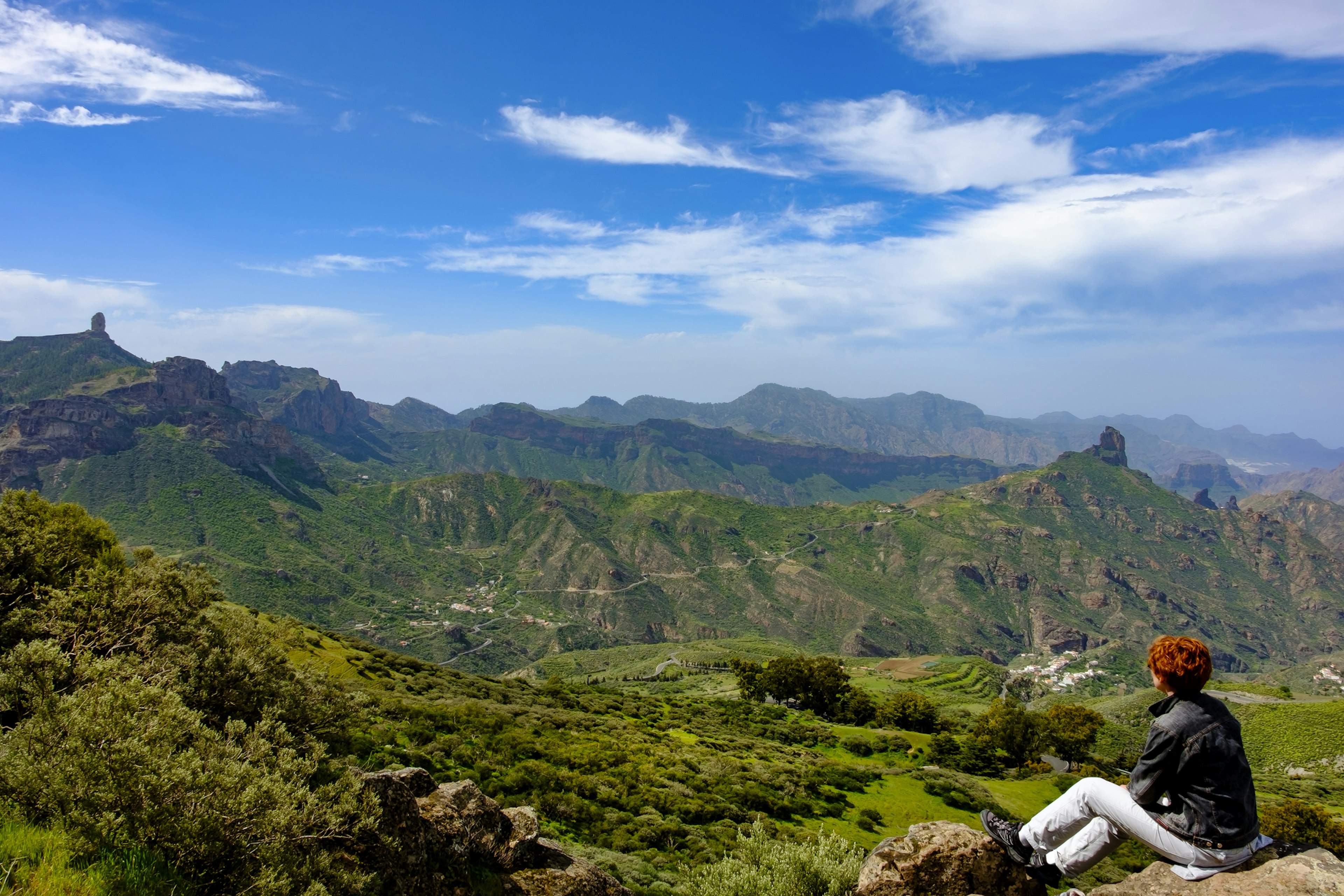 A person sits at a viewpoint over a rocky landscape with two significant outcrops rising above the rest