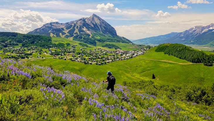 A hiker takes in a view of Crested Butte and the nearby mountains from a trail winding through wildflower fields