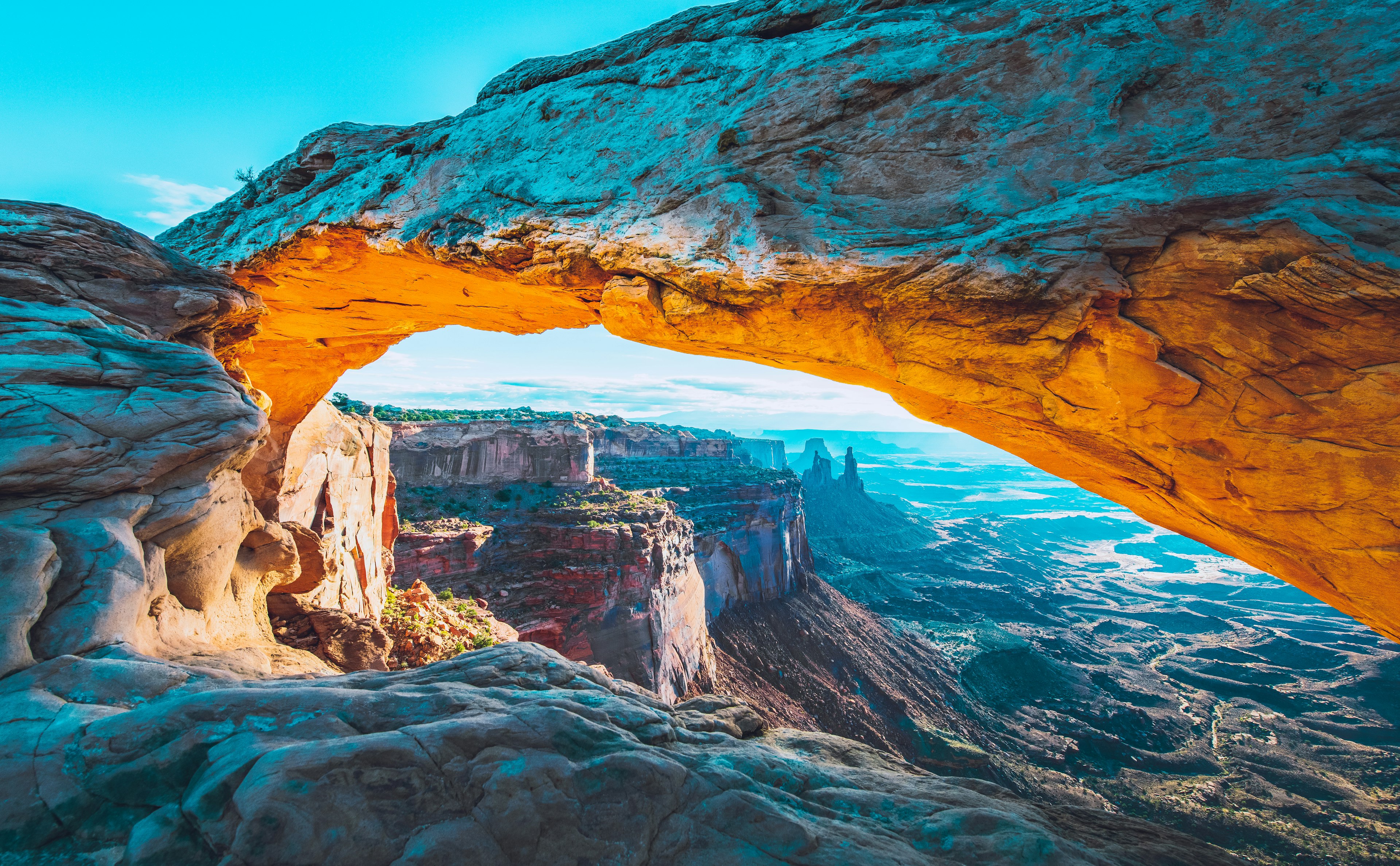 A vast red-rock archway above a landscape with needle-like pinnacles and a river far below