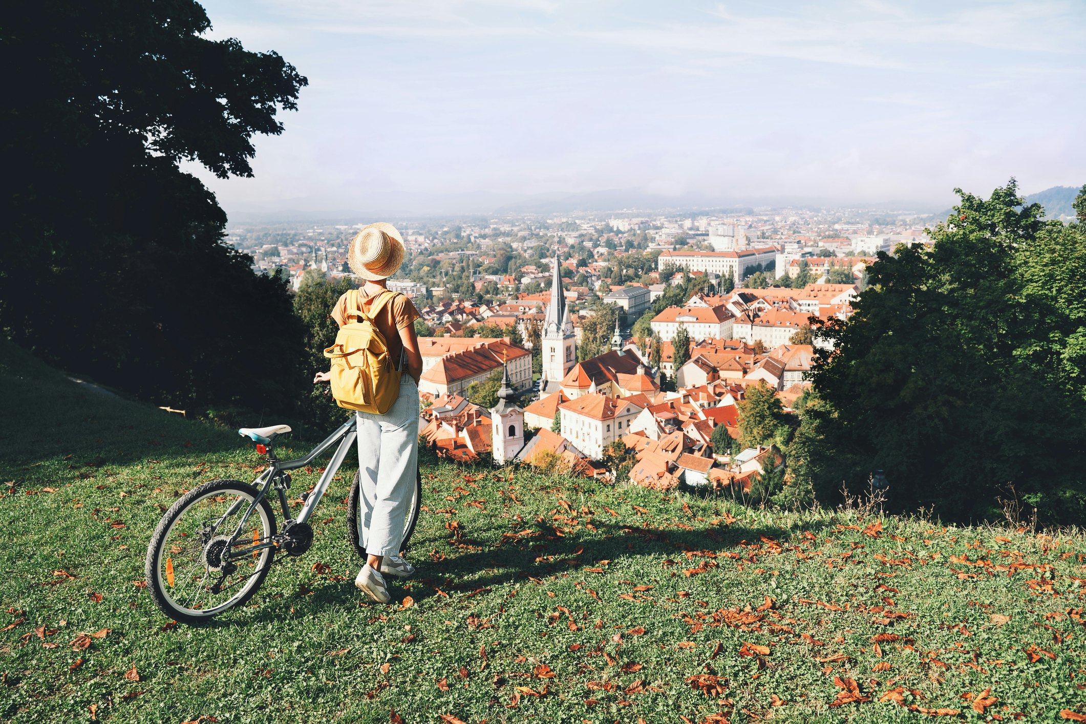 A woman standing next to her bike while looking down on the red roofs of Ljubljana from the castle grounds.