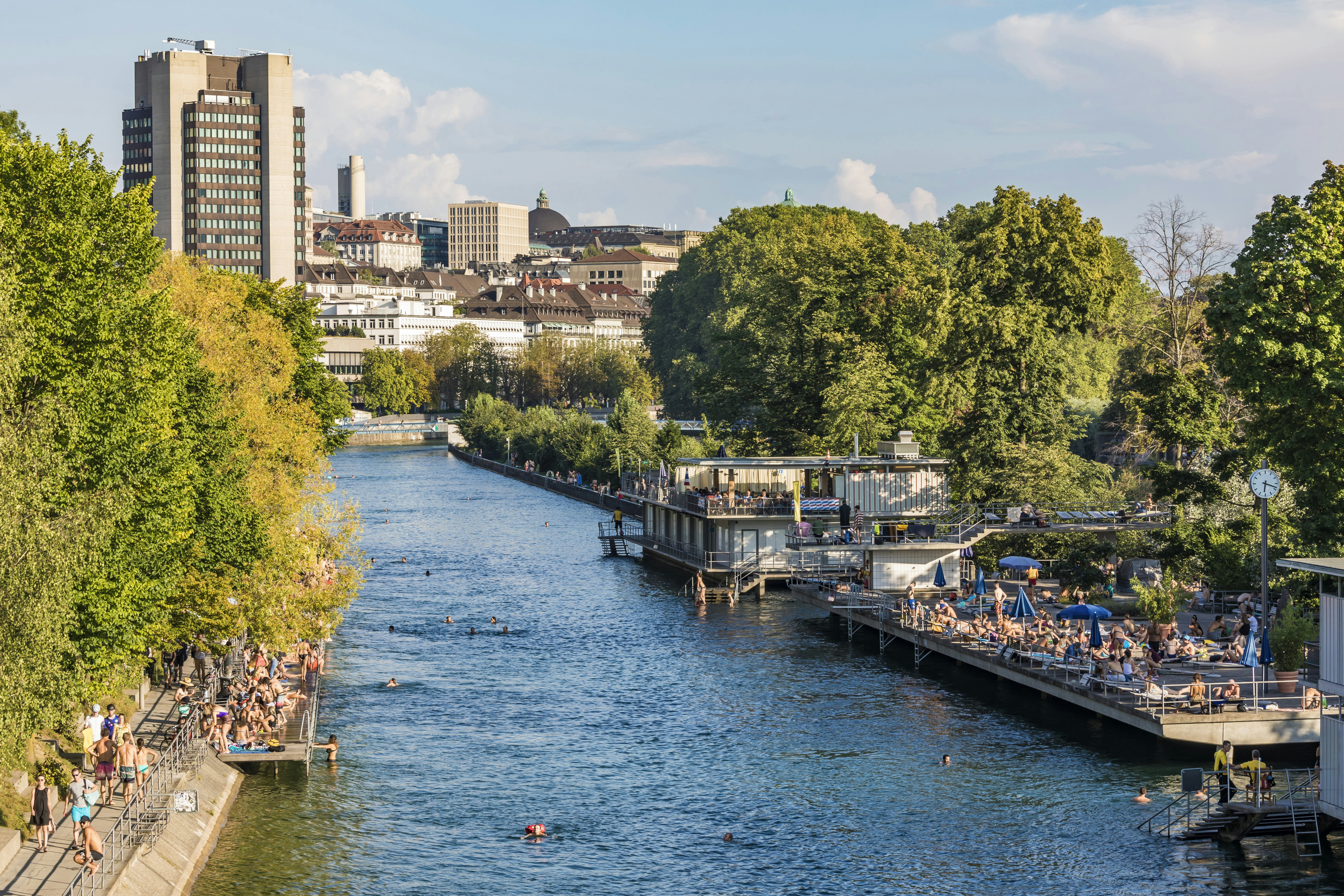 People sunbathe on decking or swim in the river that runs through Zurich