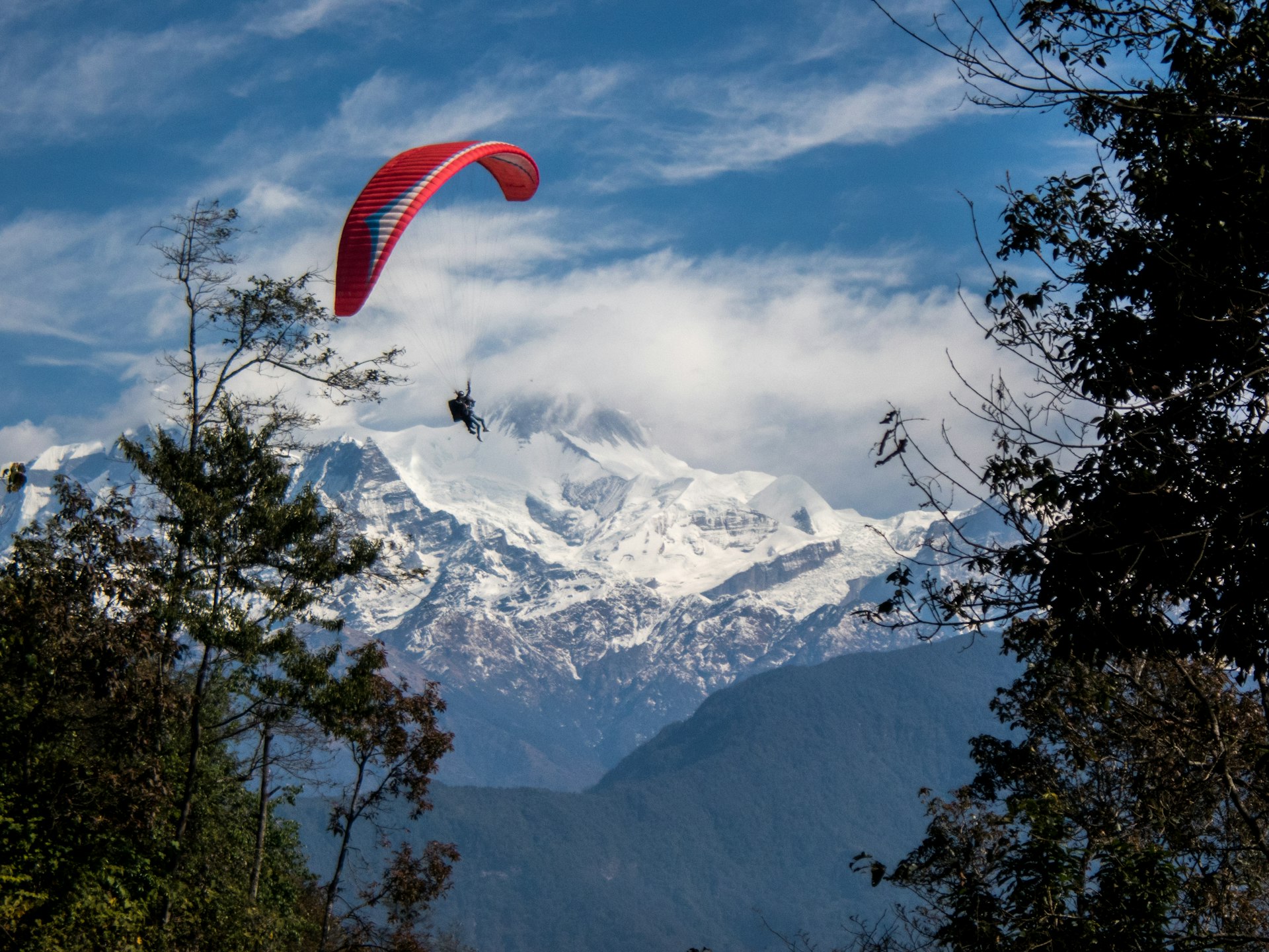 Tandem paragliders soar with the Himalaya in the background near Pokhara, Nepal