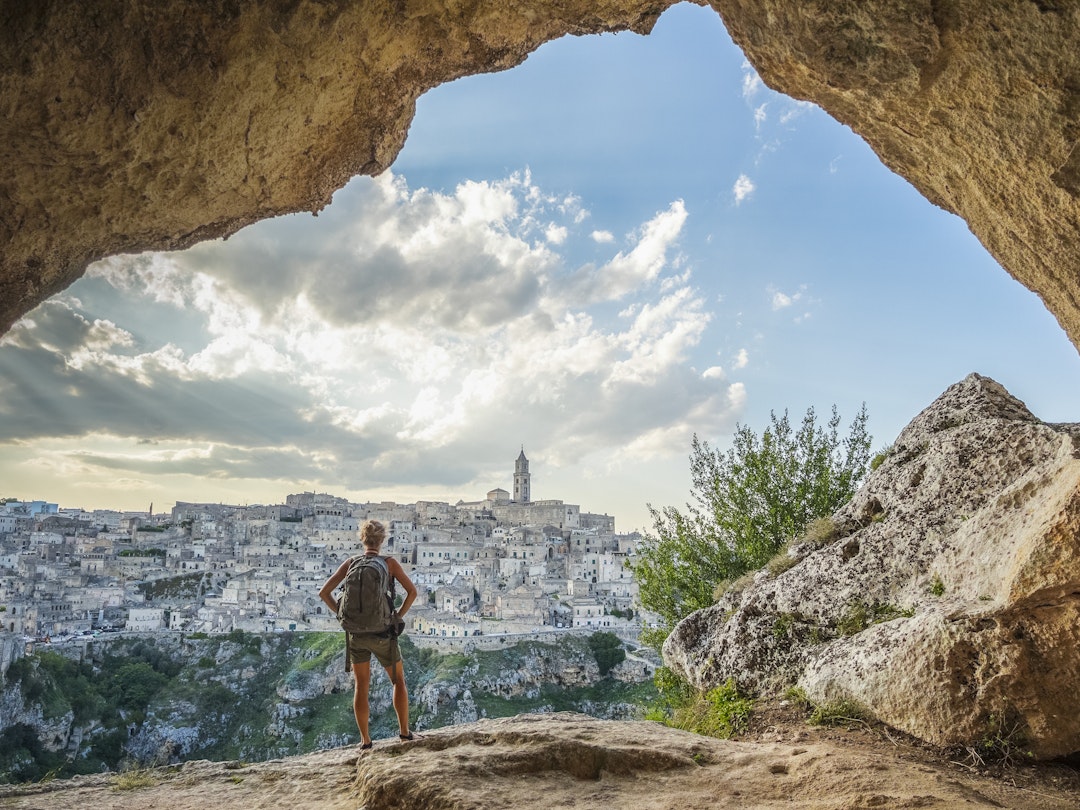 A woman wearing a backpack looking at the city of Matera from a cliff nearby, Italy