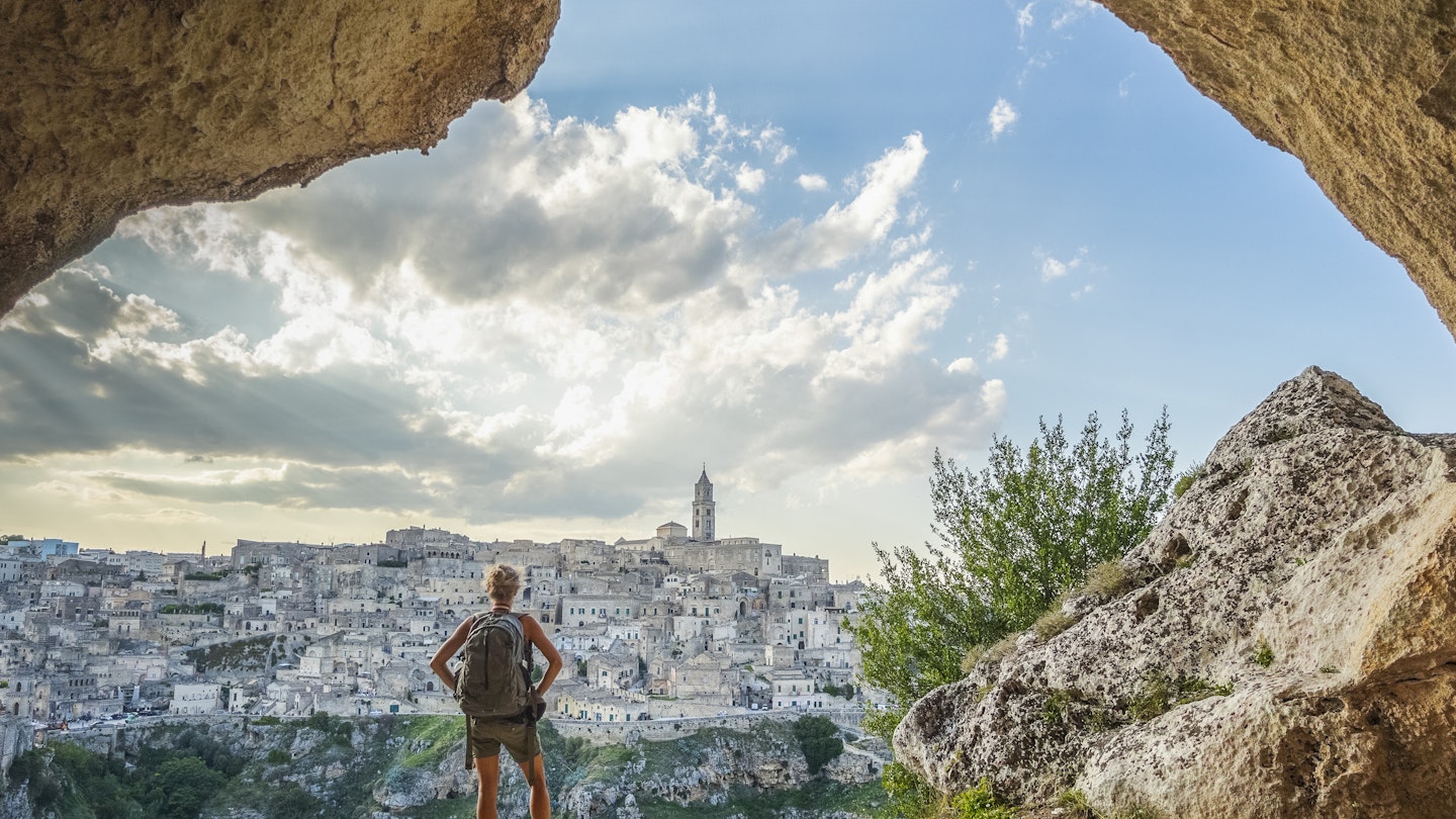 A woman wearing a backpack looking at the city of Matera from a cliff nearby, Italy