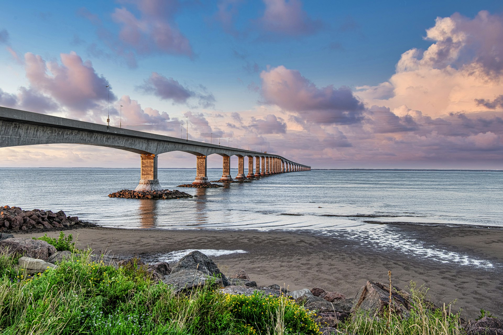 A long, narrow road bridge runs from the shoreline across the sea and stretches into the distance beyond the horizon