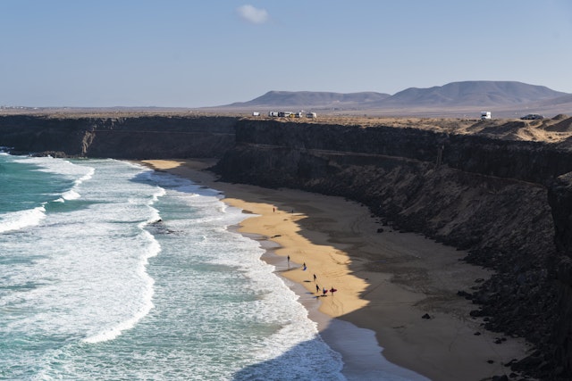 Aerial view of surfers in front of dramatic cliffs with mountains in the distance, Esquinzo beach, El Cotillo, Fuerteventura, Canary Islands, Spain