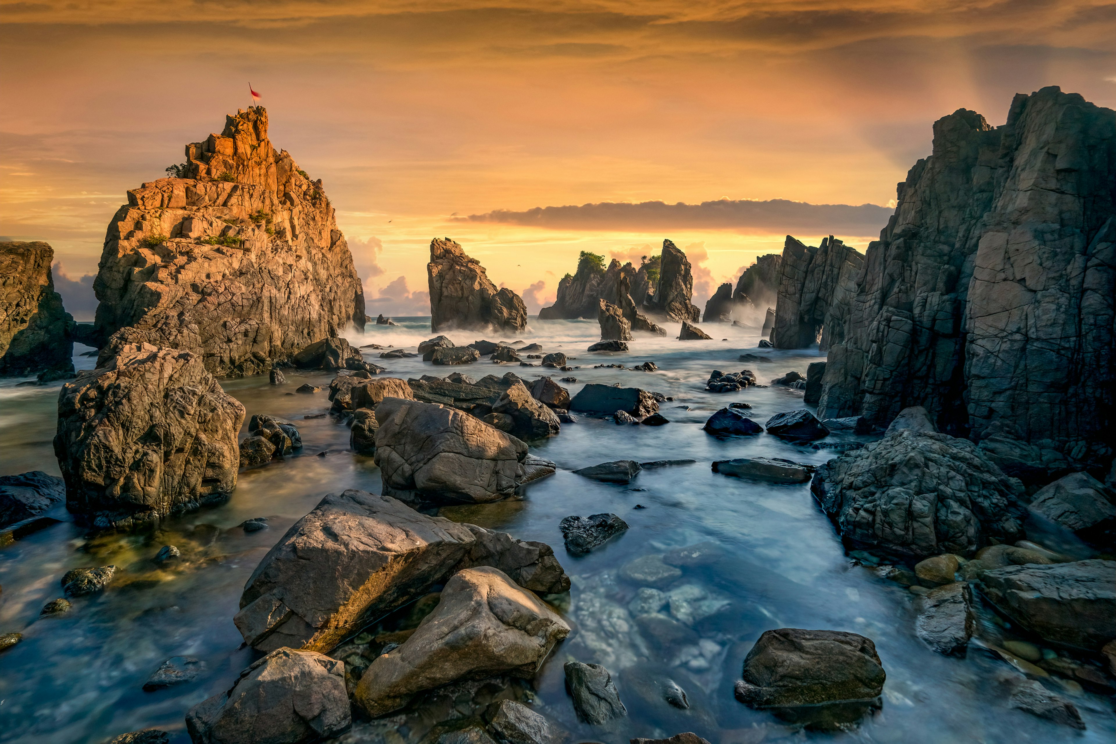 Tall jagged rocks resembling shark's teeth stand on the shore with waves crashing against them