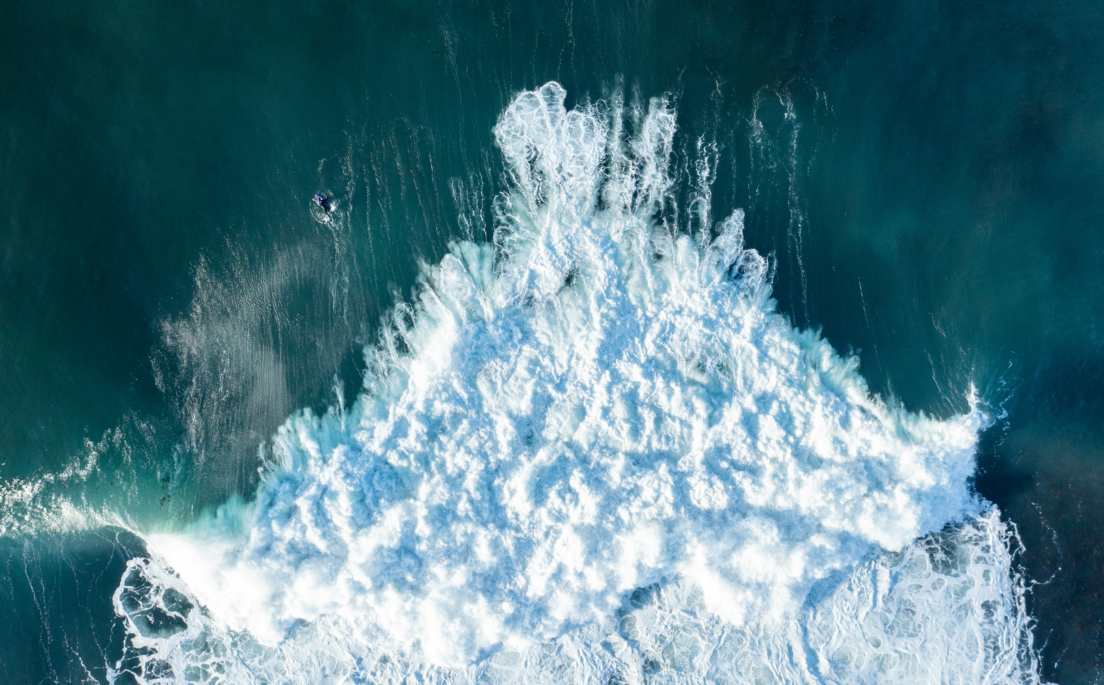 An aerial shot of wild surf with one brave surfer out near its edge