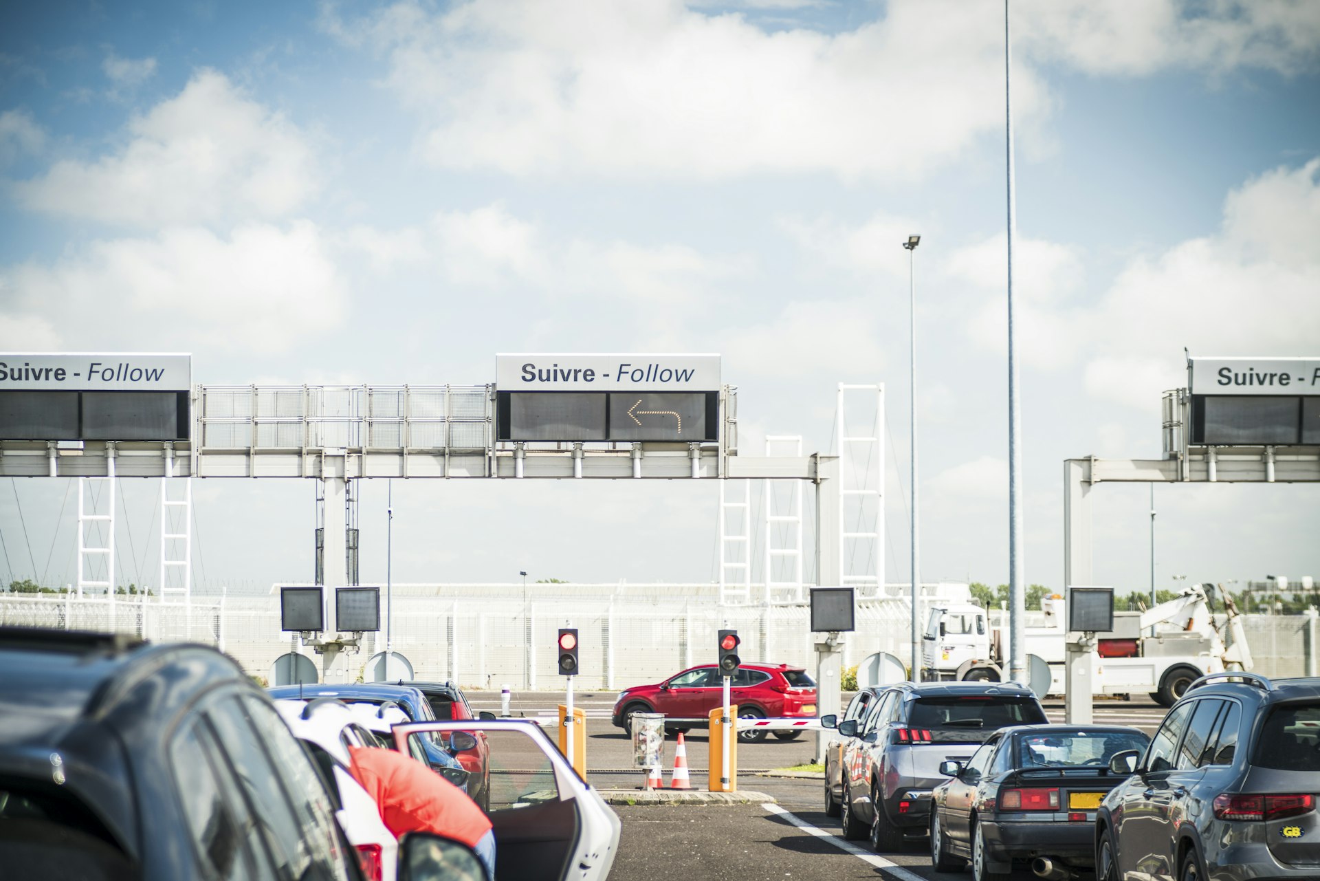 Many cars are lined up, awaiting their turn to board the Eurotunnel trains. Overhead signs direct drivers in French and English.