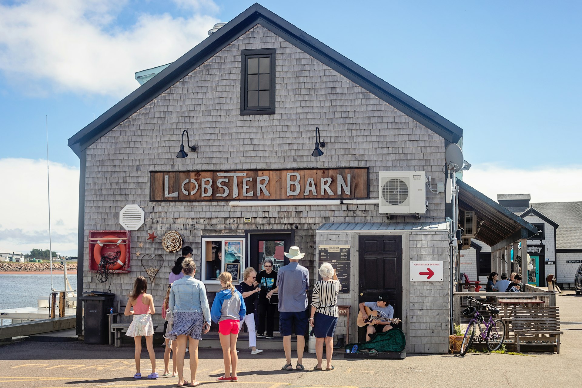 Several people linger outside a seaside lobster restaurant, where a busker is playing a guitar