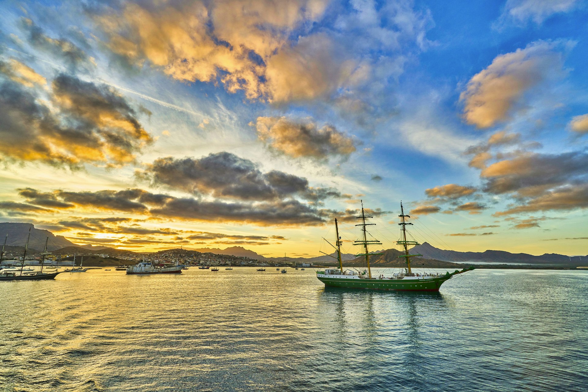 A sail boat in a bay off the coast of an island at sunset