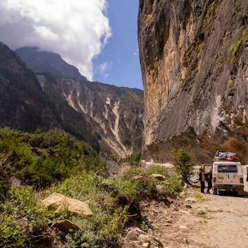 People standing by off-road vehicle on dirt road surrounded with majestic Mountain during sunny day somewhere in Nepal