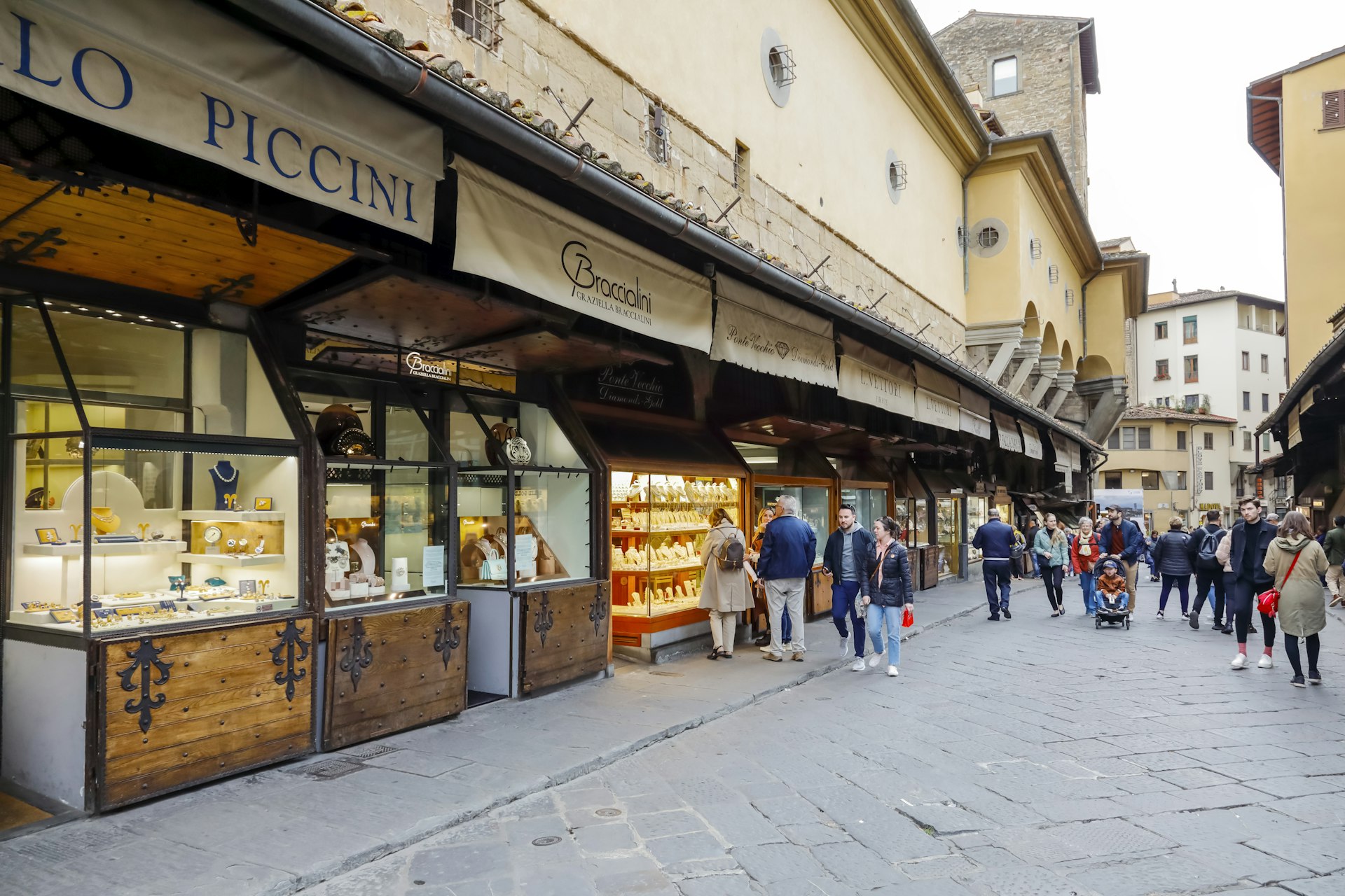 People walking along Ponte Vecchio, a medieval bridge lined with shops selling high end goods such as jewelry