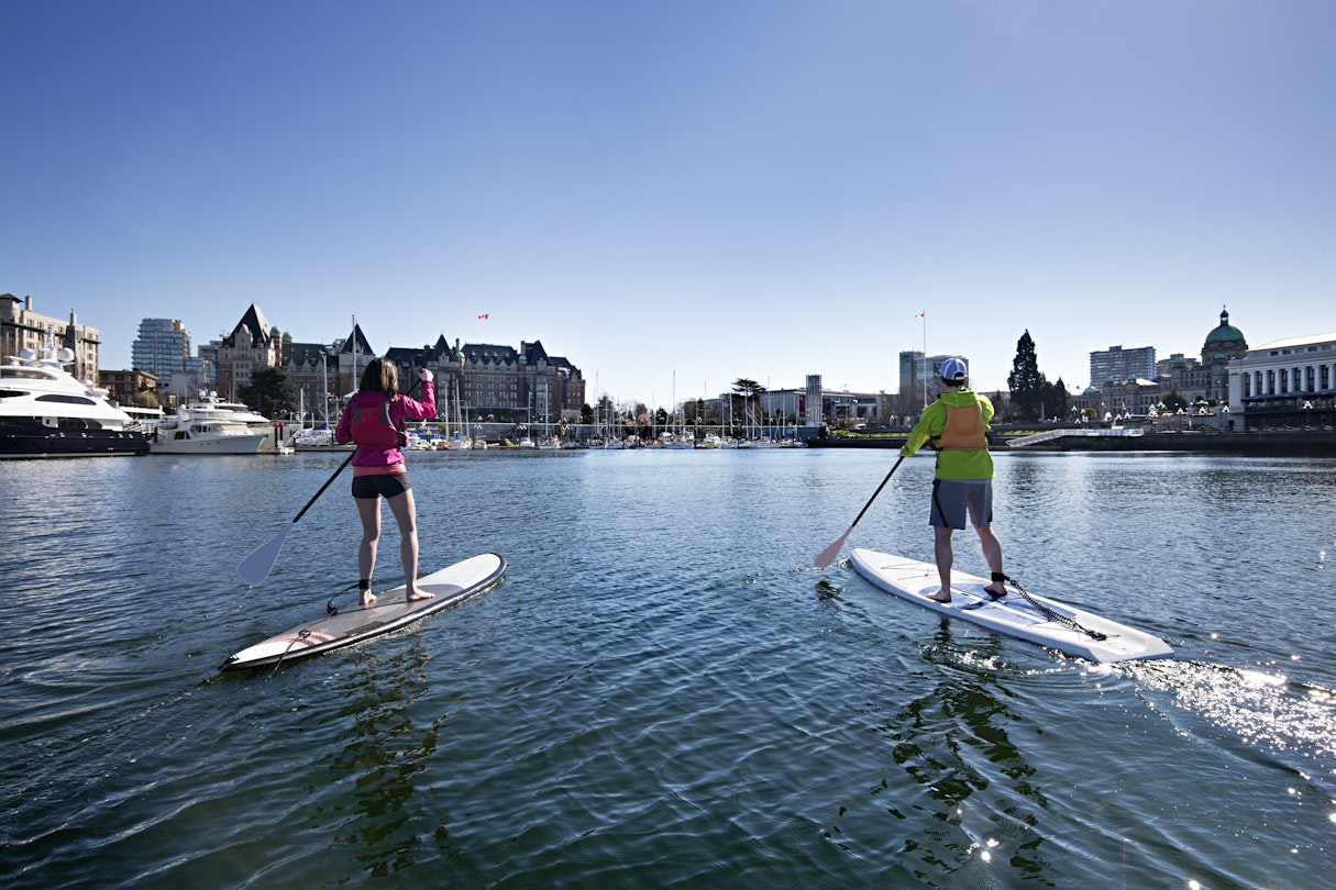 Man and women paddle stand up paddleboards through the Inner Harbour towards the Parliament Buildings. © Aaron Black / Getty Images RFC