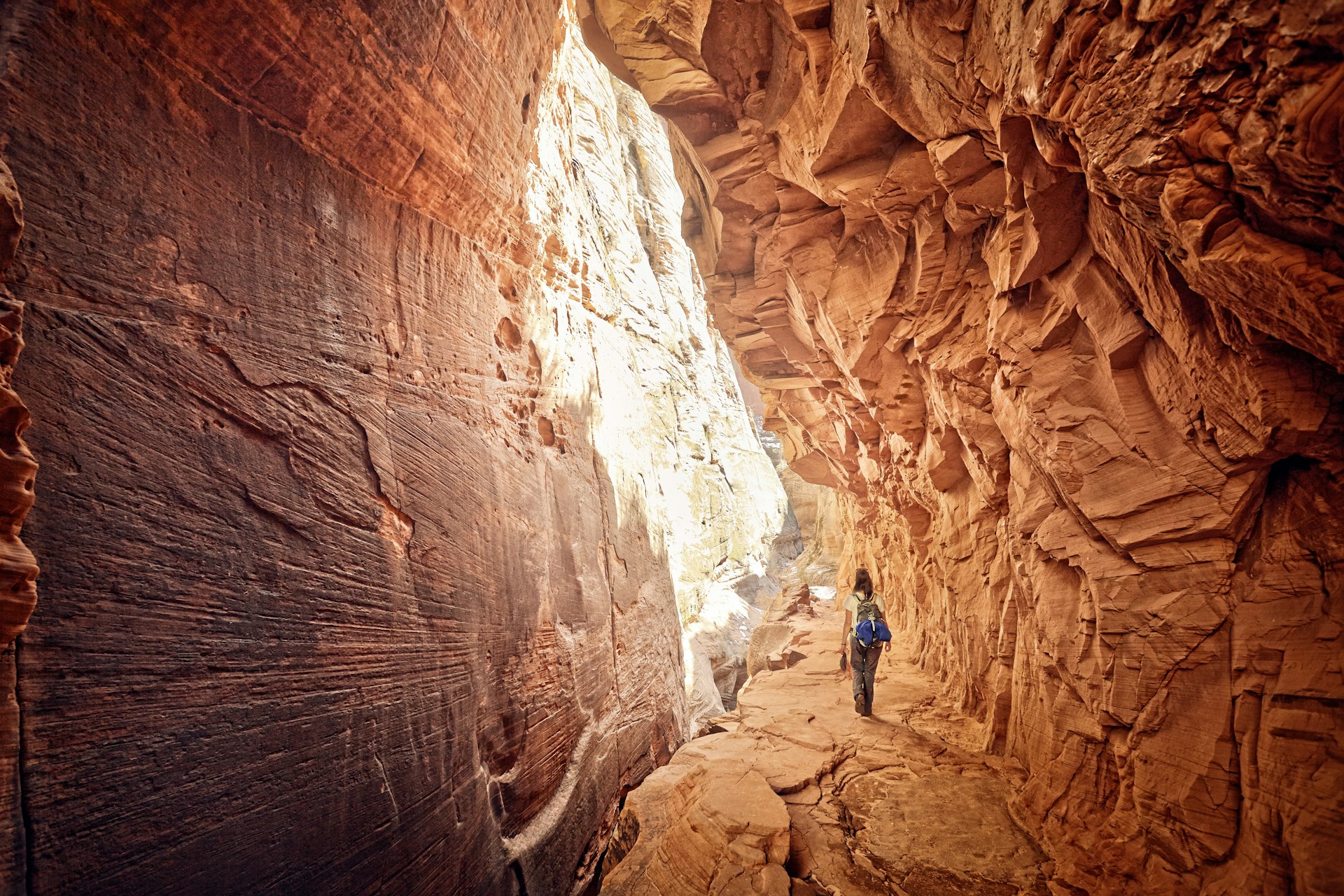 A woman hikes through a narrow canyon with tall red-rock walls either side of her