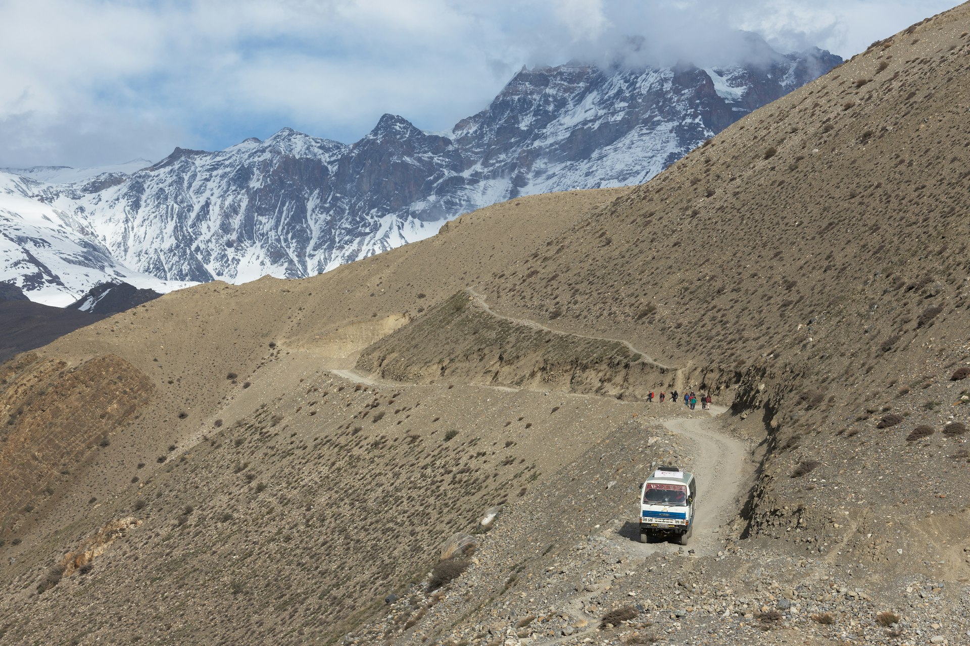 A bus seen from above with the Himalayas in the distance on the dusty road between Jomsom and Muktinath, Nepal