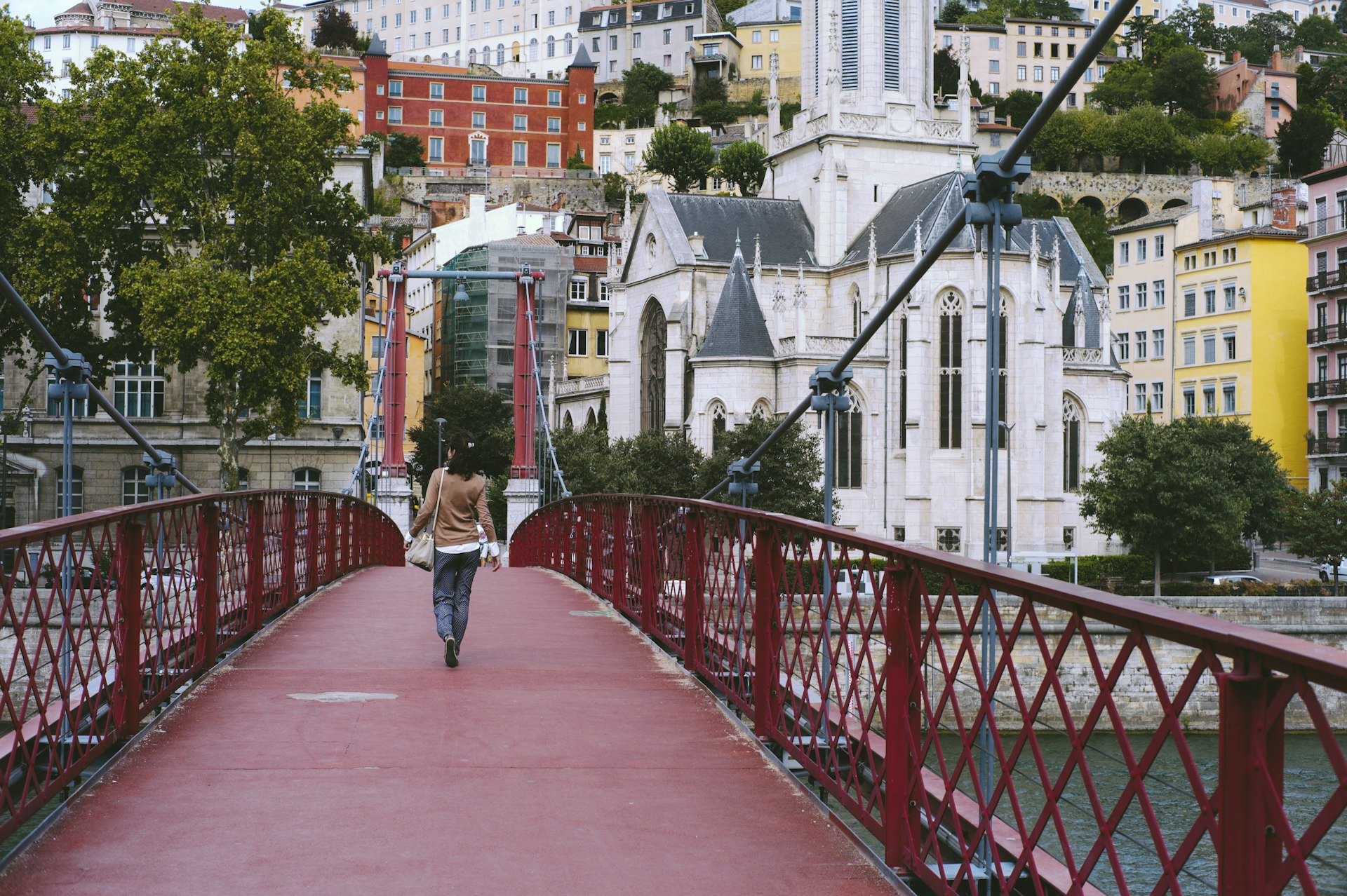 A woman walking on a red footbridge over the Saône river in Lyon