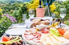 Brettljause, traditional cold plate with meal, cheese, vegetable, bread and a bottle wine with glasses in garden © Photoflorenzo / Getty Images