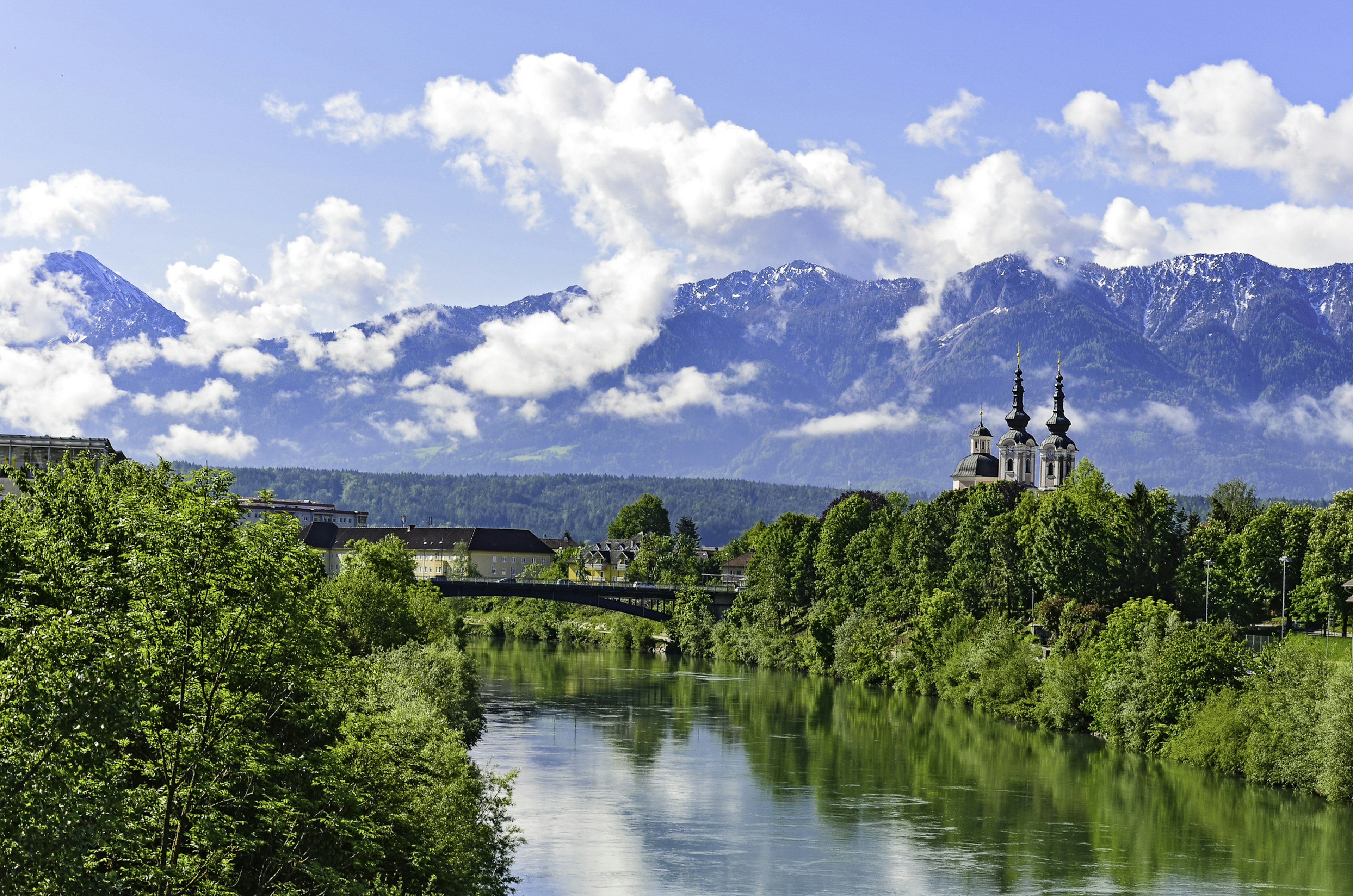 A mountain range in the clouds with a small chapel on the bank of a river