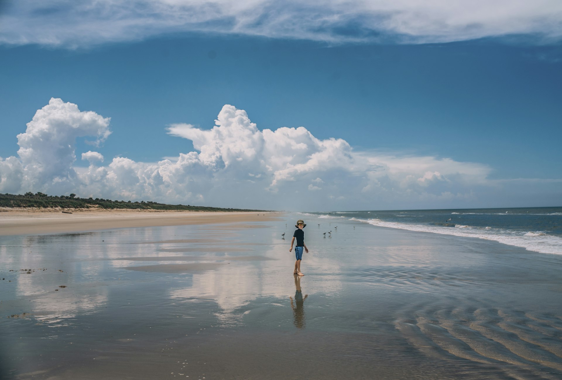 A boy stands on a wet expanse of sand at New Smyrna Beach, near Orlando, Florida