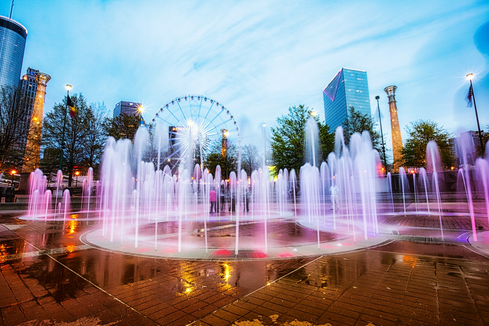 Fountains in the shape of the Olympic Rings shoot water upwards at Centennial Olympic Park at dusk