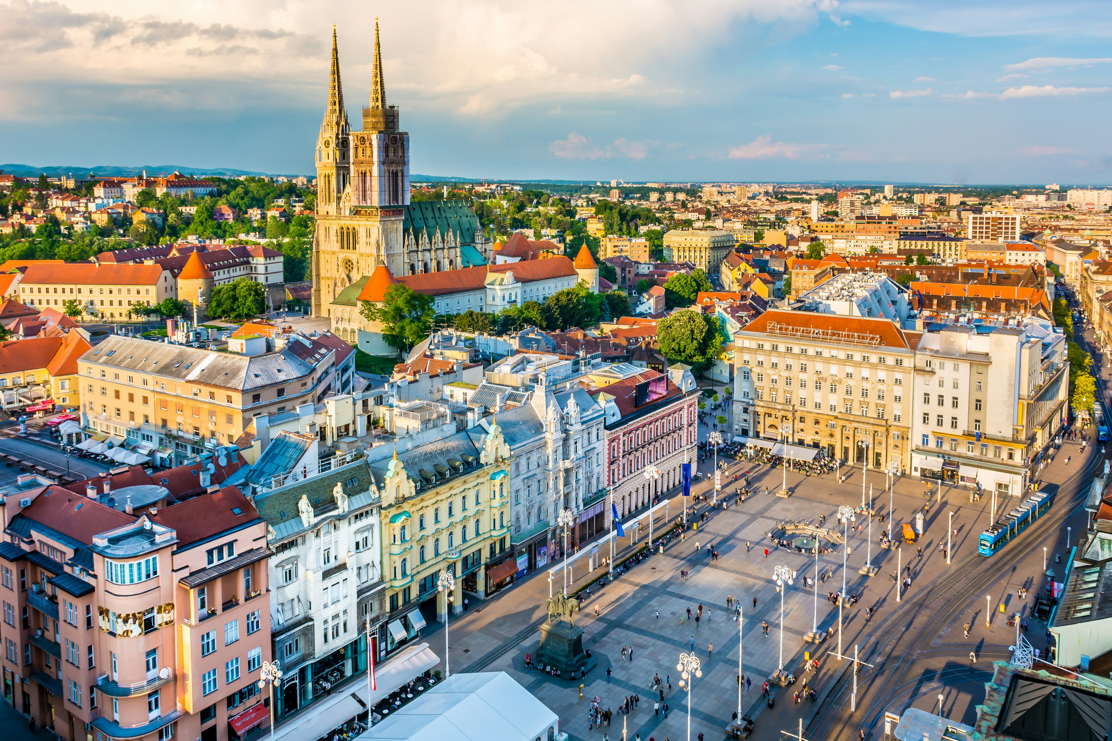 A large city square surrounded by pastel-colored buildings and a skyline dominated by a Gothic-style cathedral