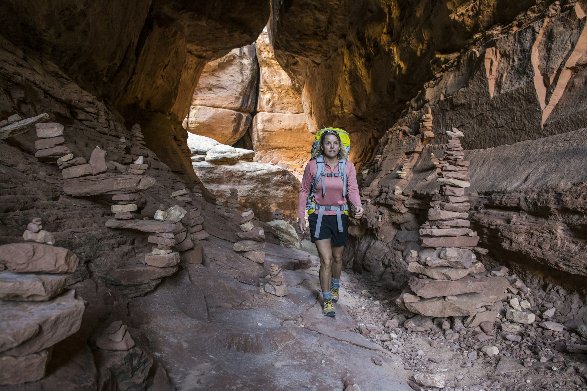 A woman backpacking past stone cairns on the Joint Trail in the Needles District of Canyonlands National Park, Monticello, Utah