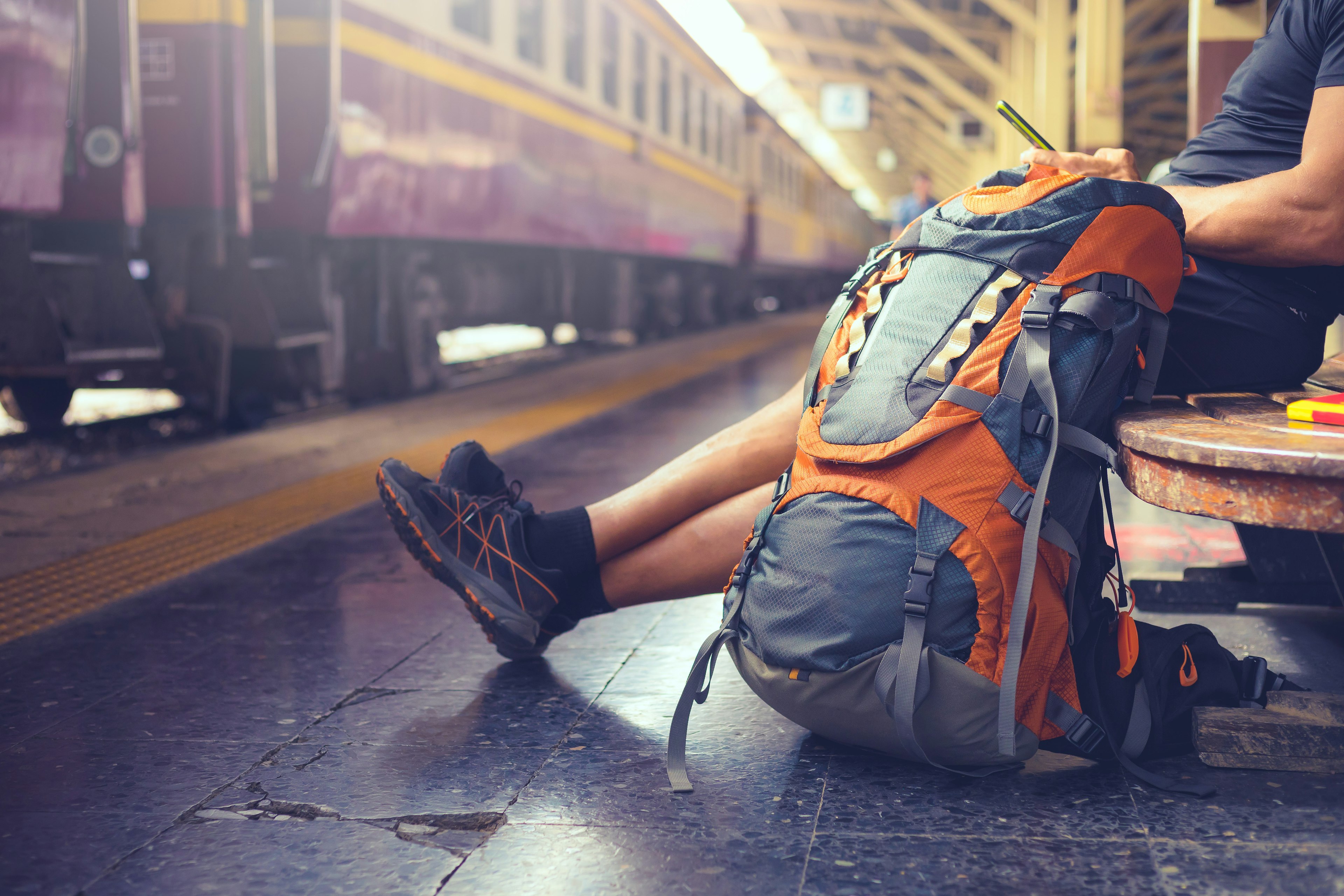 A backpacker uses a cell phone at a railway station while waiting for a train