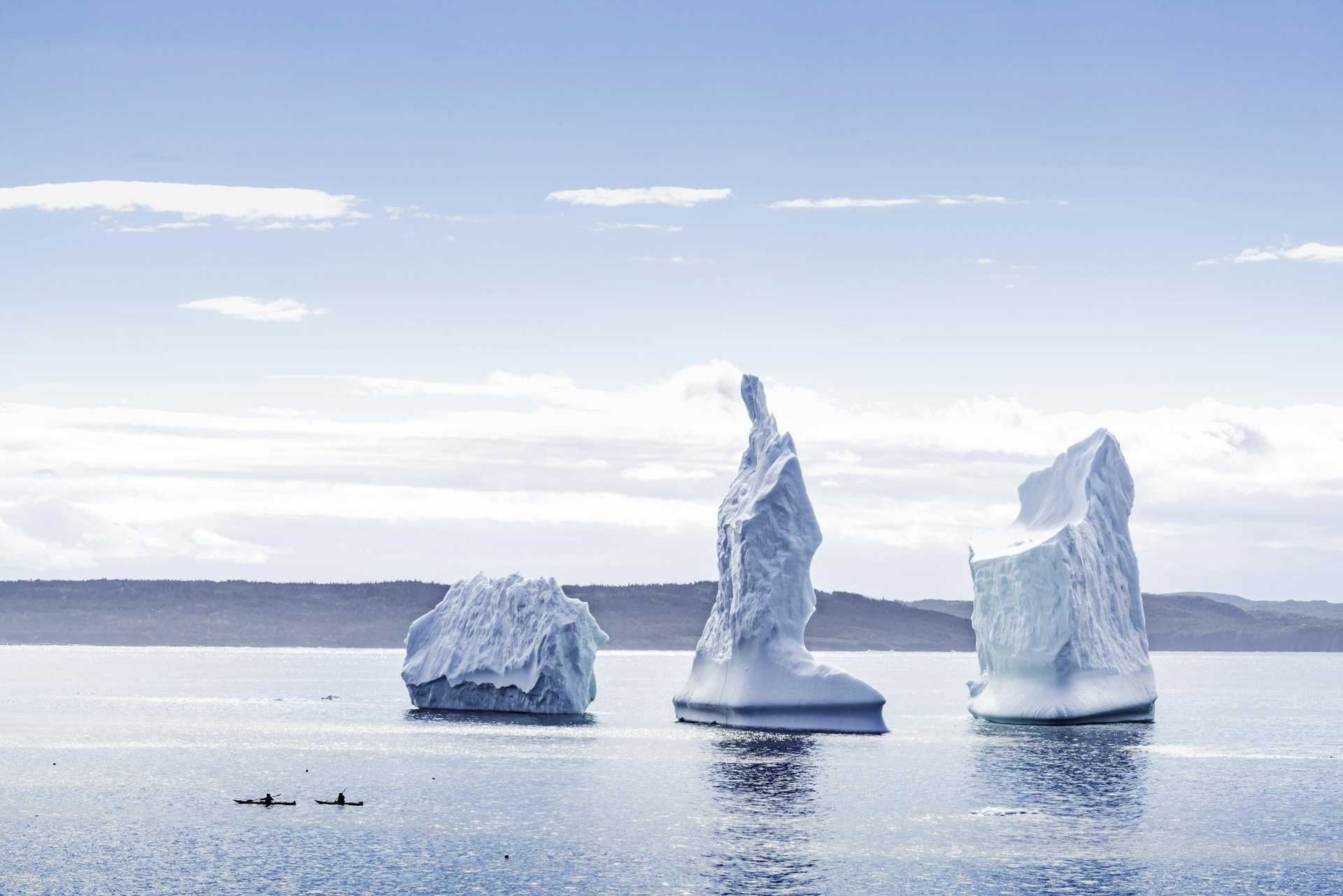 Two kayakers paddle past icebergs in the Wolf Cove of Bonavista, Newfoundland, Canada