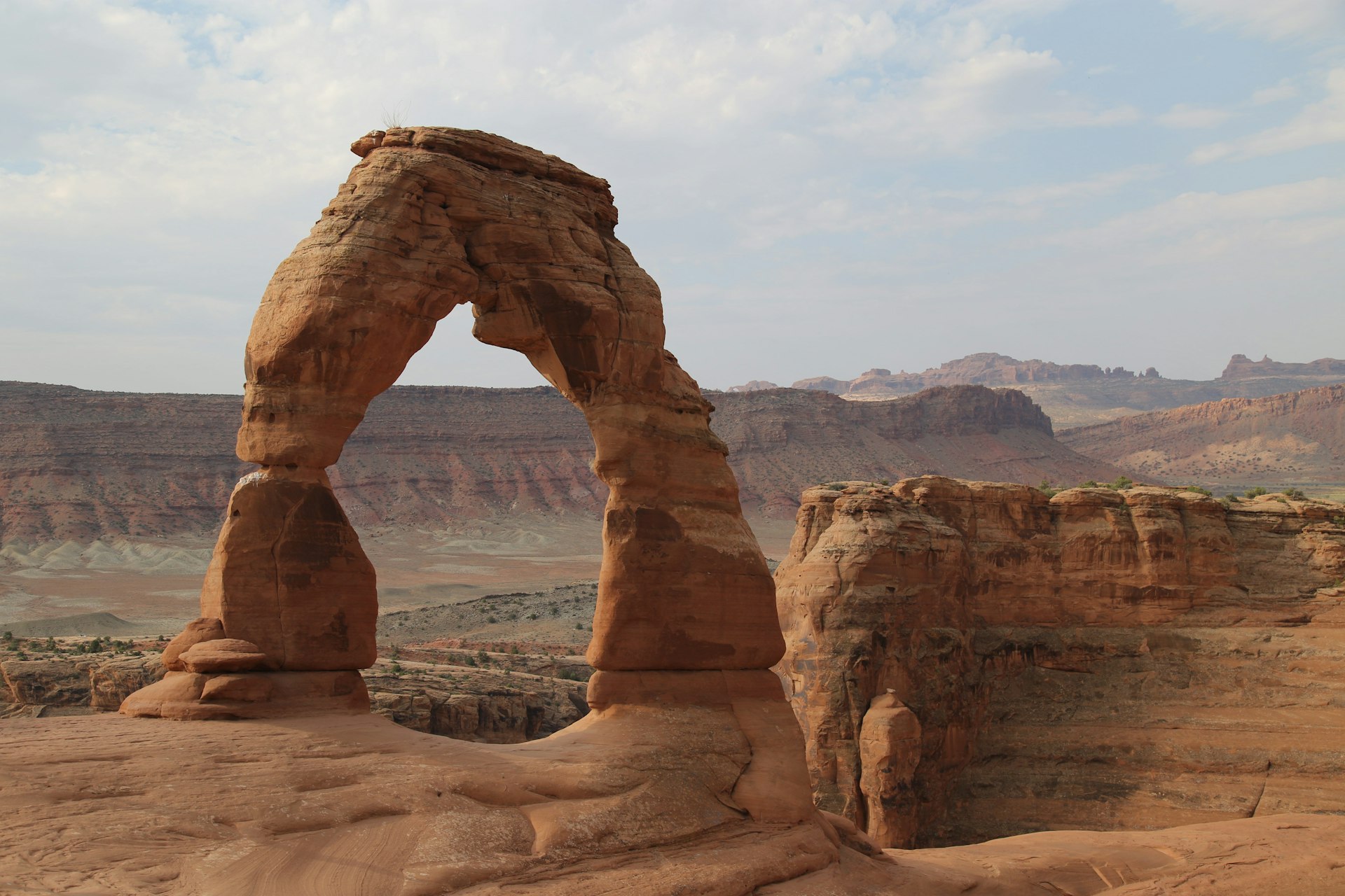 A sandstone arch with red rock cliffs in the background under a blue sky