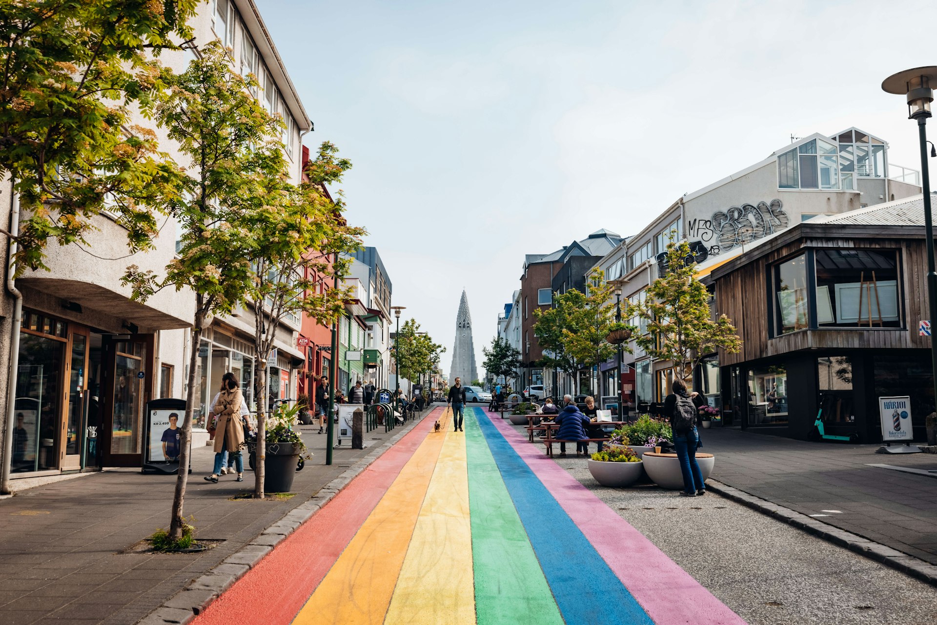 A street, with a walkway of striped rainbow colors, leads to the pointed spire of a cathedral 